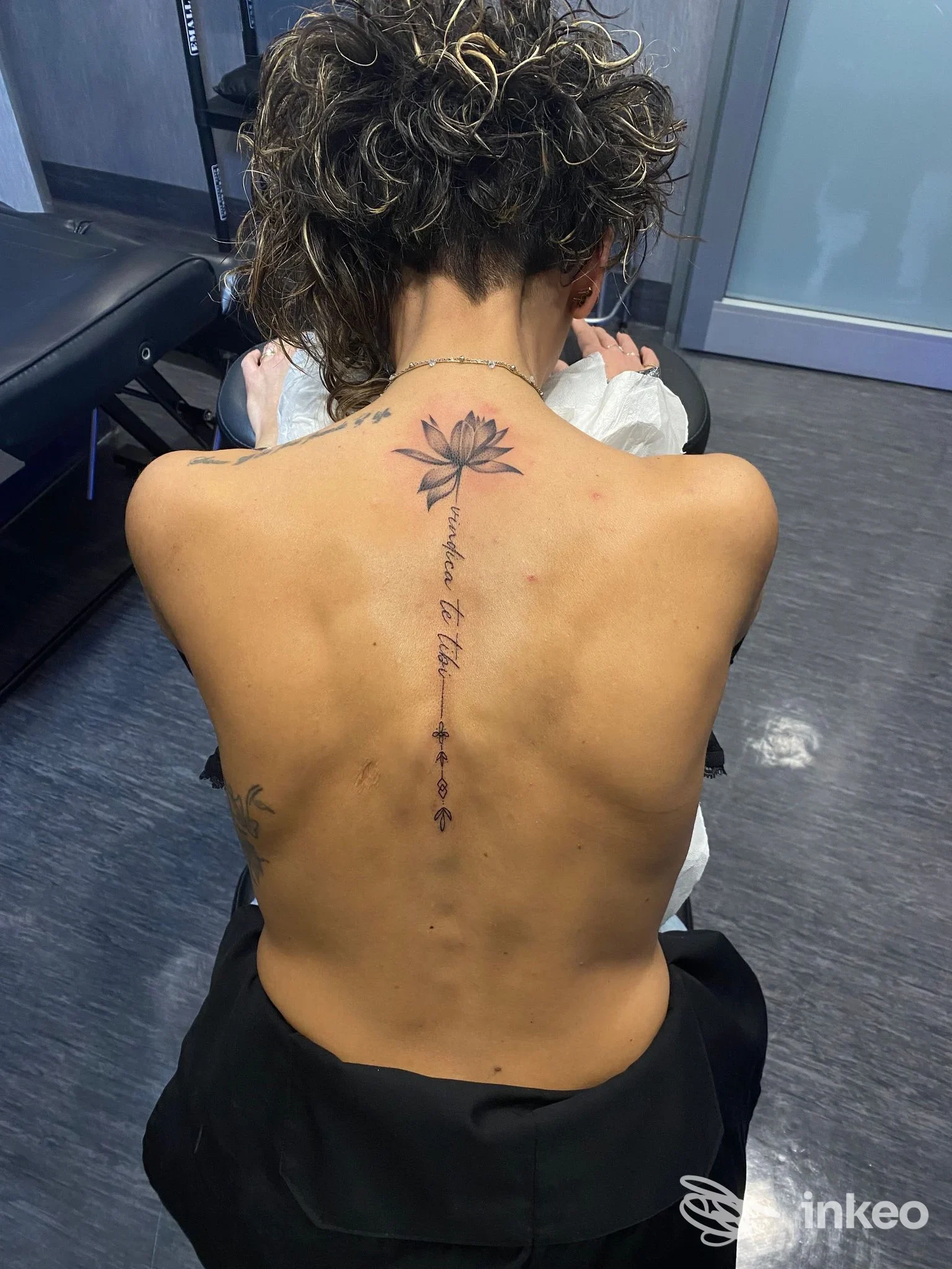Tatuaggio visibile lungo la colonna vertebrale di una persona, con un fiore sulla schiena e un dettaglio a catena di piccoli motivi, senza mostrare il volto.
