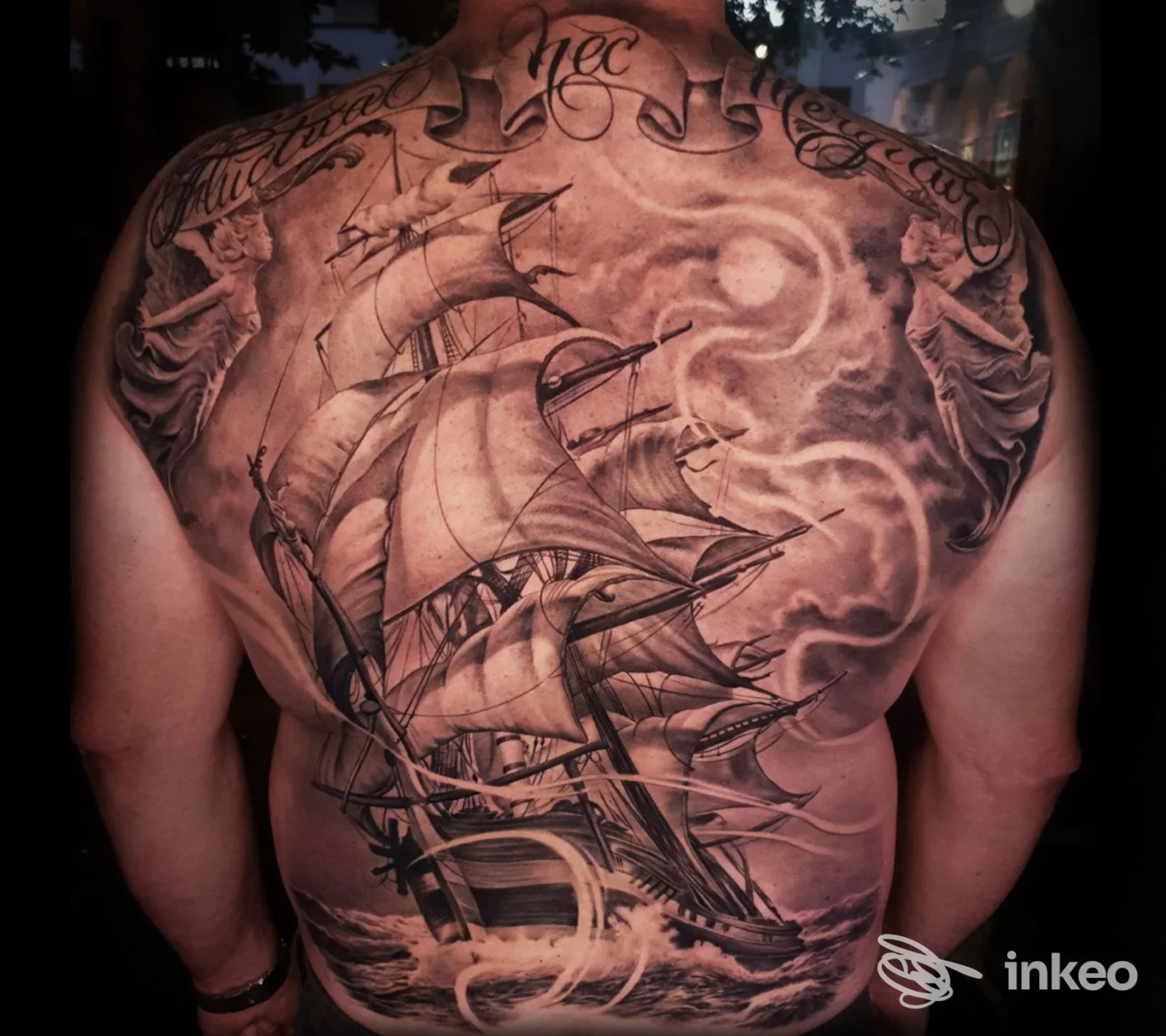 Schiena di un uomo completamente tattooata con un veliero dettagliato tra onde e nuvole, tatuaggio realistico coprente la superficie dorsale.