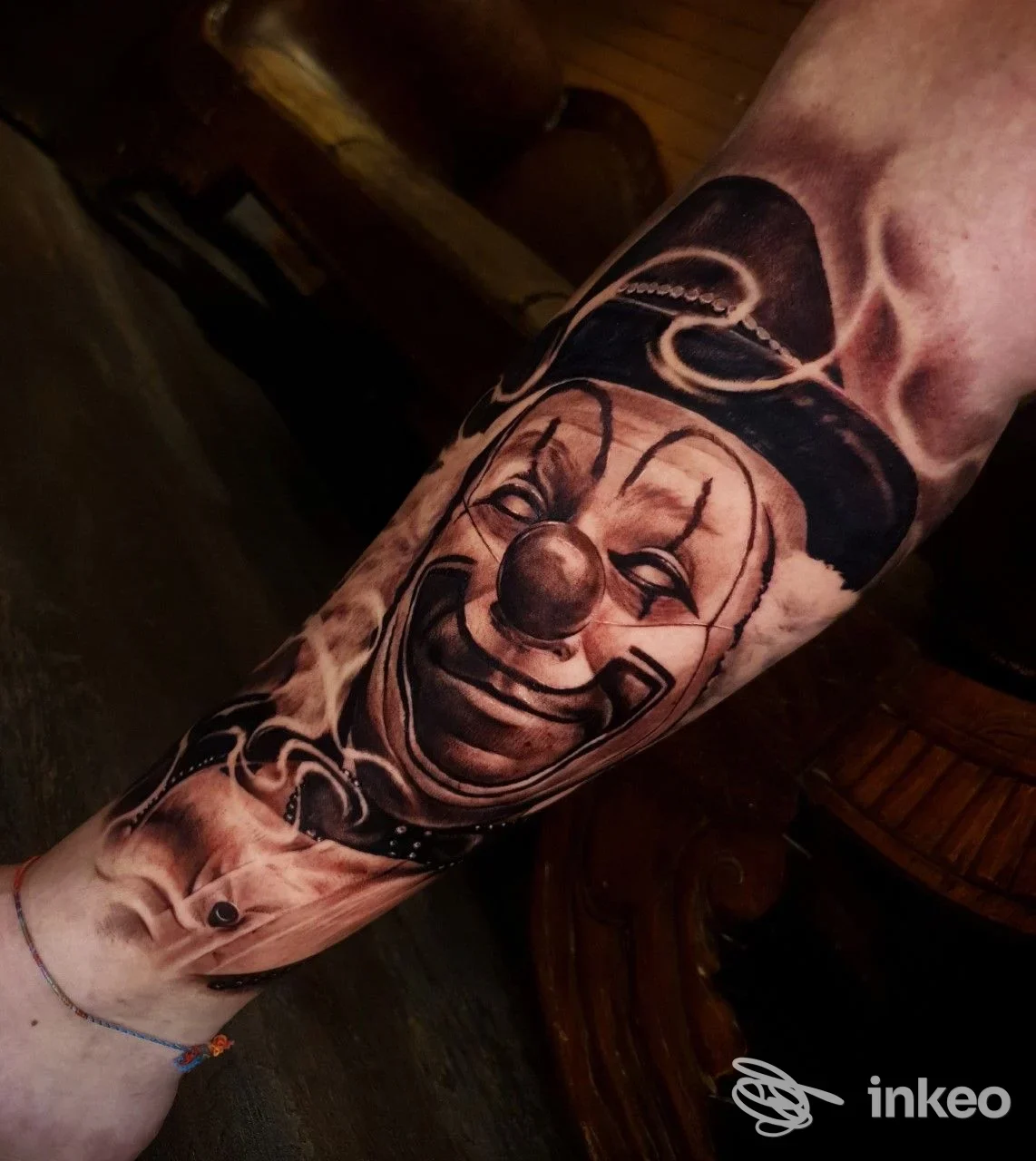 Avambraccio sinistro raffigurante un tatuaggio realistico in bianco e nero con un volto di clown, eseguito su pelle reale; nessuna grafica di social, nessuna immagine su schermo