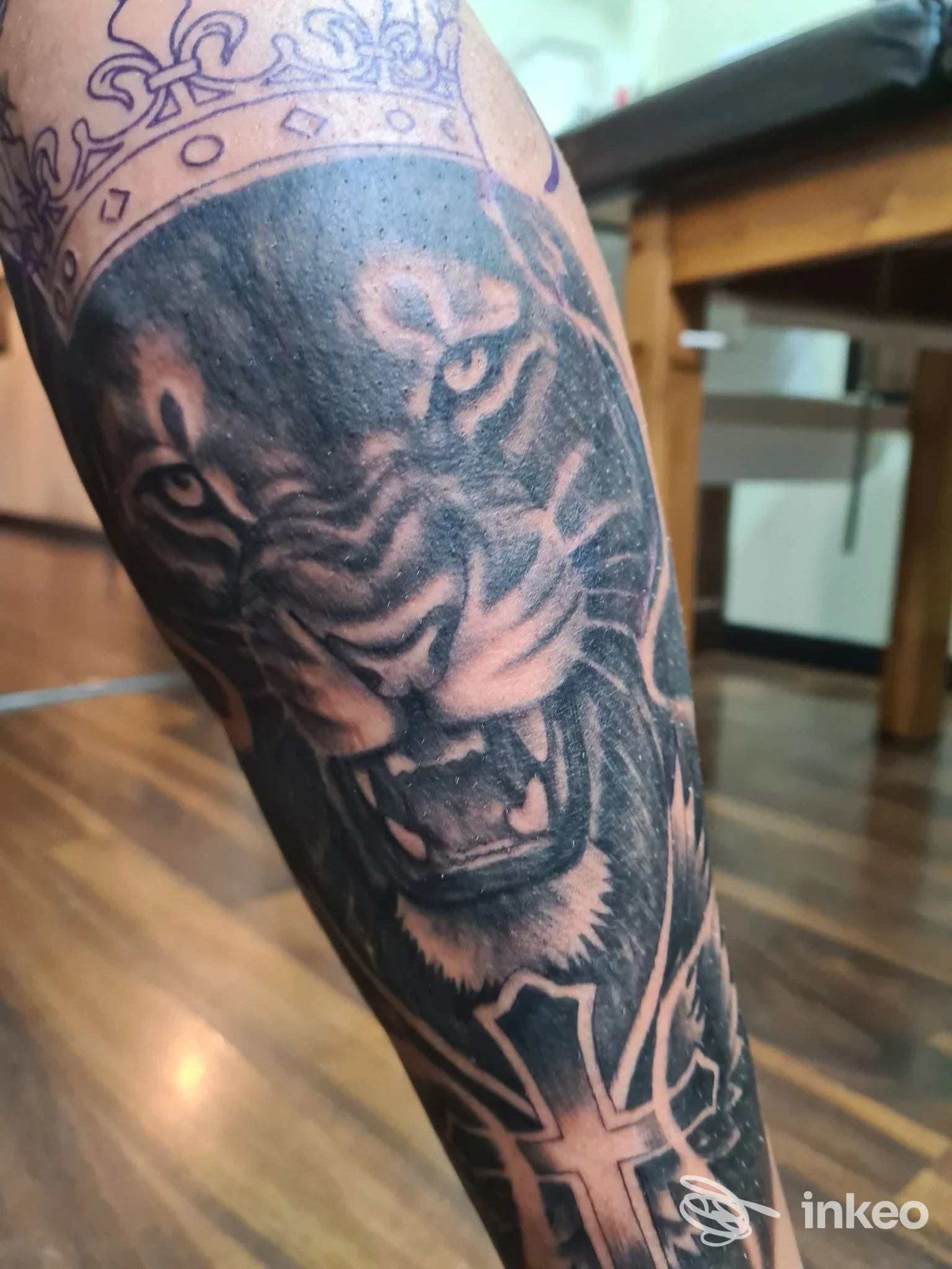Dettaglio di tatoo su pelle: un leone scuro con zanne minacciose e corona, tatuato sull'avambraccio.