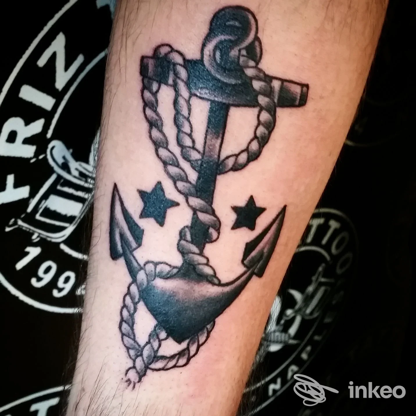 Tattoo su pelle raffigurante ancora con cima intrecciata, nacre d'ancora e corde, braccio visibile, stile tradizionale, colori in nero/grigio.