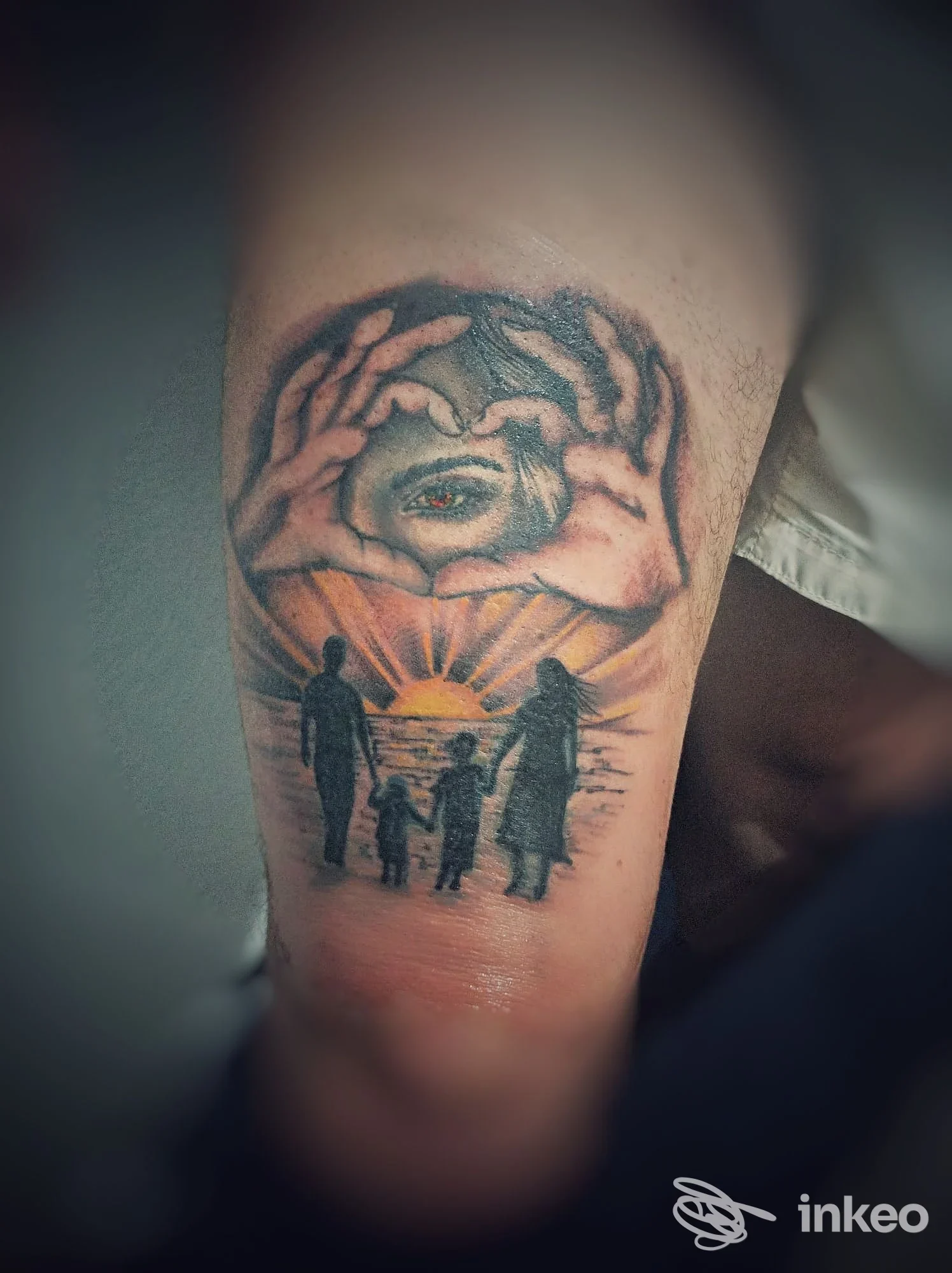 Tattoo sull'avambraccio raffigurante una scena familiare al tramonto: mani che circondano un occhio centrale, colori vividi e linee nitide.