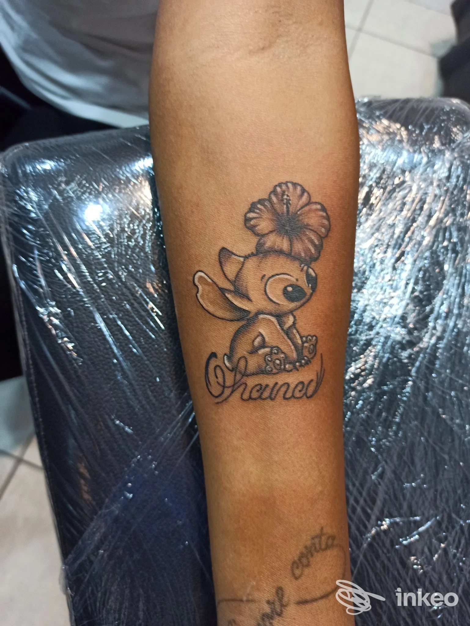 Avambraccio con tatuaggio realistico di un personaggio con fiore in testa, eseguito su pelle; stile fumetto, colori neri e dorati.