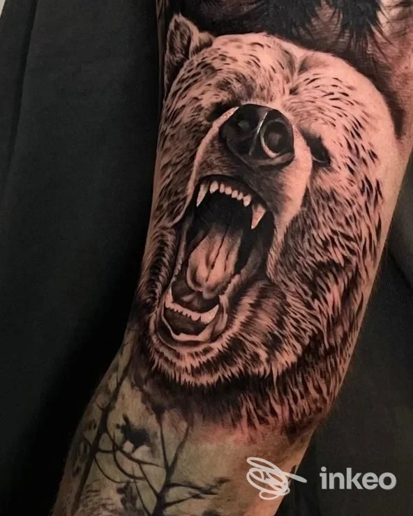 Tattoo realistico di orso bruno sulla parte superiore del braccio, eseguito in tonalità nero/grigio con dettagli accurati della bocca aperta e dei denti.
