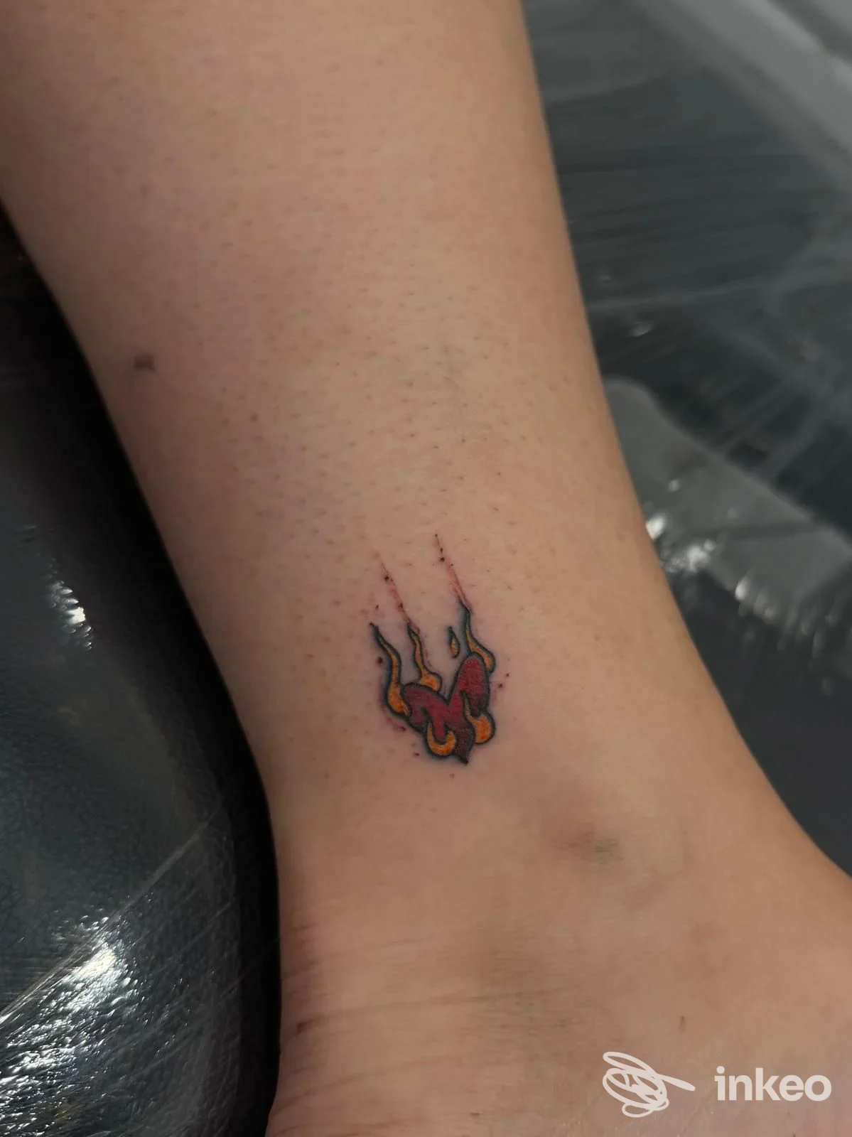 Piccolo tatuaggio a forma di fiamma colorata sulla caviglia di una persona, tatuaggio ben definito sulla pelle.
