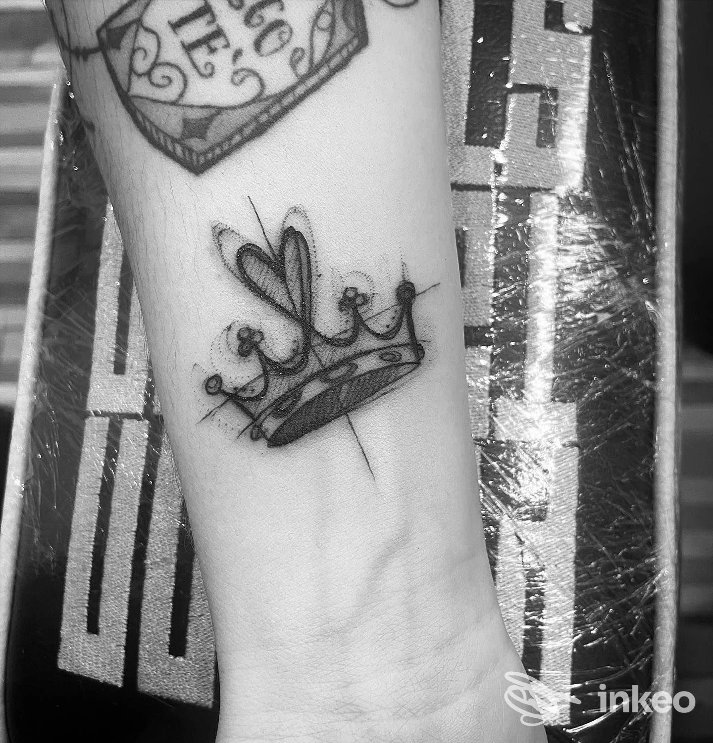 Polso/nell’avambraccio si vede un tattoo a tema corona con cuori e dettagli stilizzati in toni scuri, parte di un braccio con altri tatuaggi visibili.