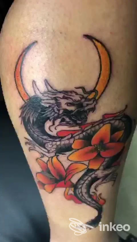 Tatuaggio reale su pelle: drago stilizzato in bianco e nero con fiori arancioni, senza elementi social o schermi visibili, visibile completamente sul braccio.