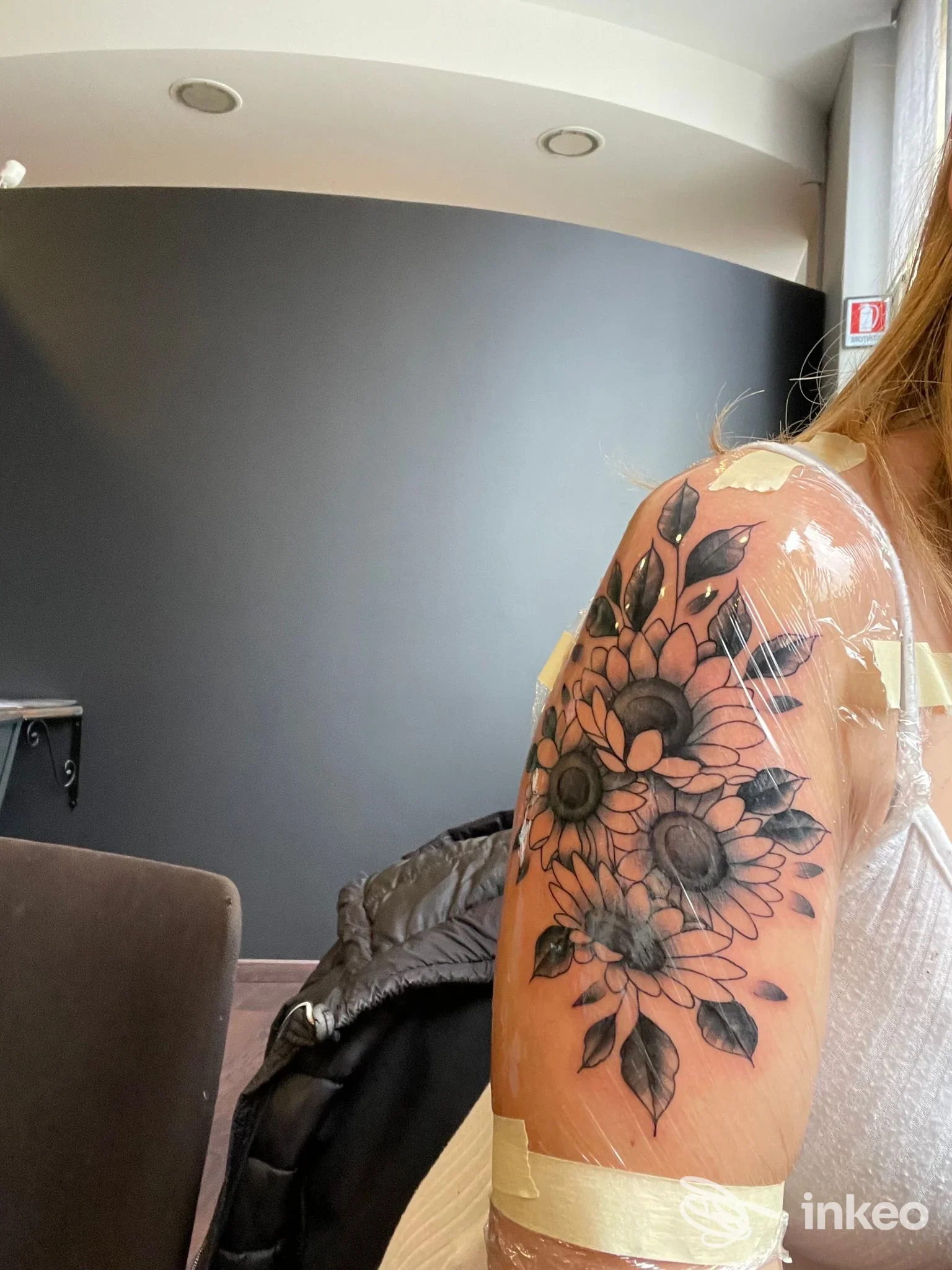 Tattoo visibile sulla spalla di una persona: bouquet di girasole nero-grigio con dettagli di foglie, realizzato da Le Officine Tattoo Studio a Laveno-Mombello