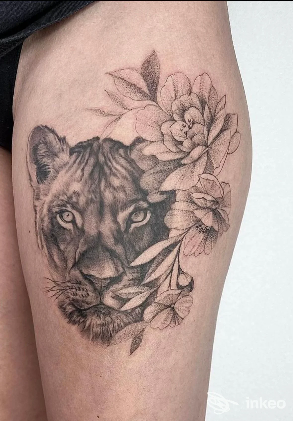 Tatuaggio realistico in bianco e nero di una tigre con fiori sulle merci della gamba, realizzato sulla pelle; studio Le Officine Tattoo Studio, Laveno-Mombello.