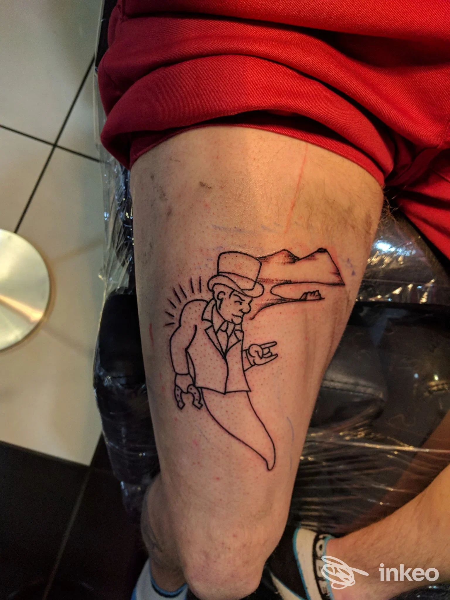 Tattoo sul braccio raffigurante un uomo in completo con cappello e sfondo montagnoso, realizzato sul corpo del soggetto.