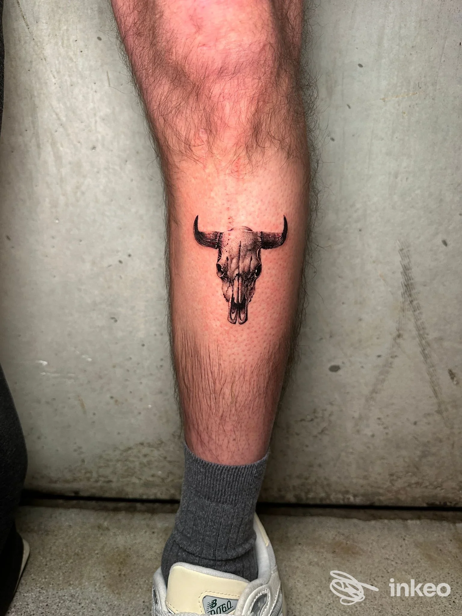 Tatuaggio realistico di un teschio di toro sul polpaccio di una persona, tono scuro e linee nette, pelle vistosamente liscia.