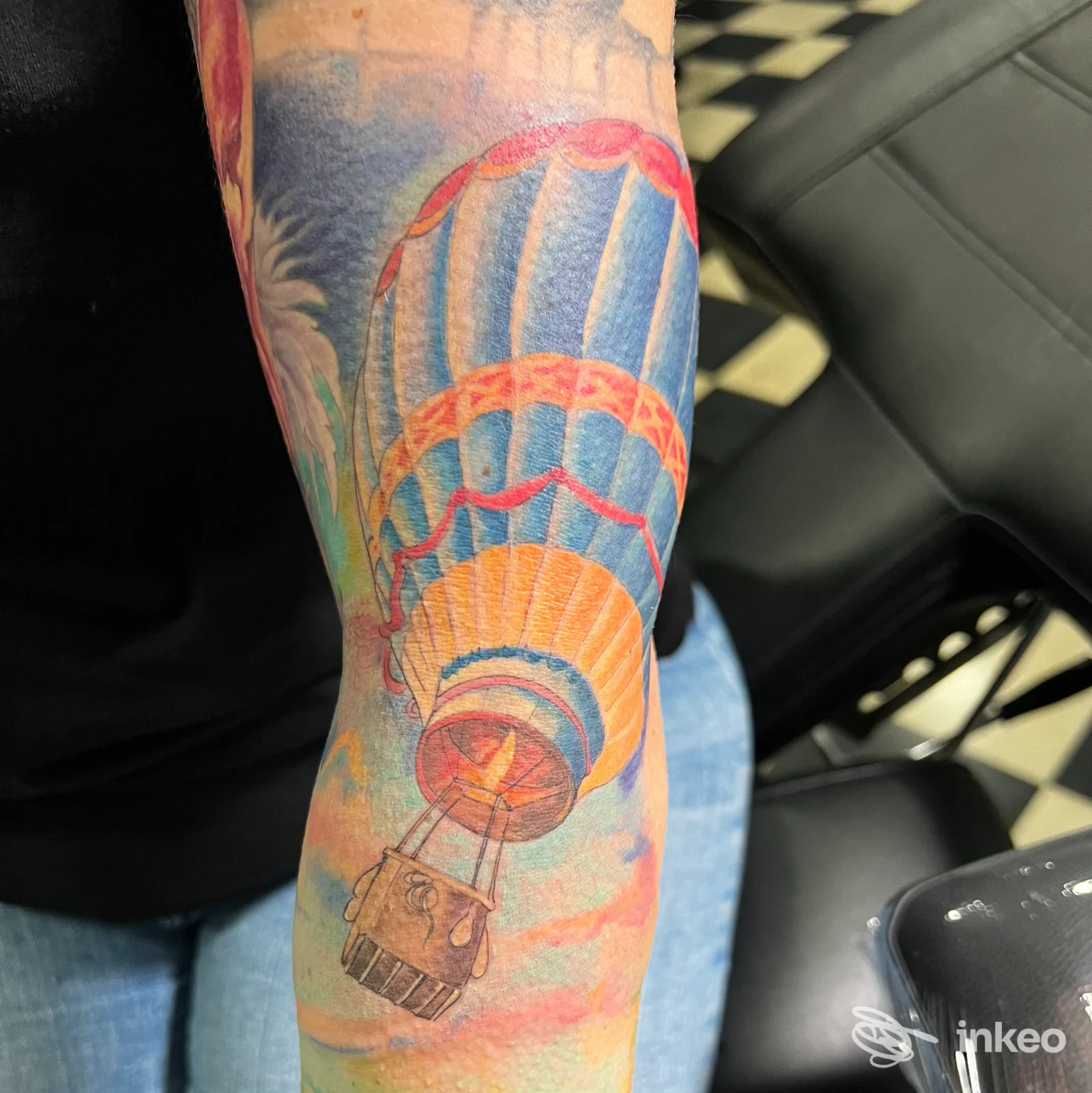 Piercing colorato su braccio con anguiforme paracadute e sfumature azzurre e rosse, tatuaggio pienamente visibile sulla pelle.