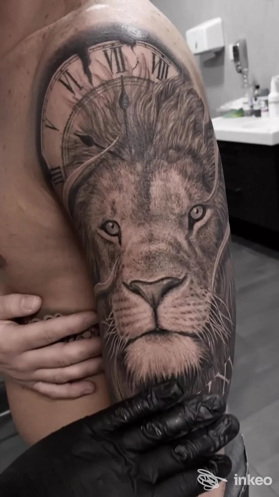 Tattoo realistico di leone con orologio romano sul braccio, eseguito su pelle, tono in bianco e nero.