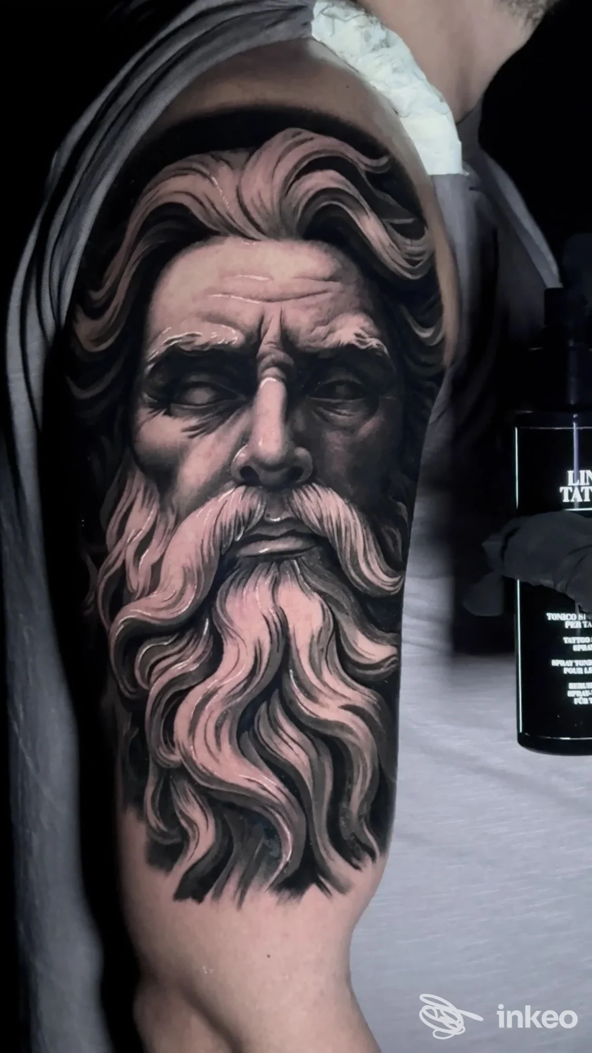 Tattoo sul braccio raffigurante un volto barbuto con lunga barba, realizzato dal tattoo studio LOTO INK TATTOO SHOP a Frattamaggiore, colori scuri e tono grigio. Ritratto realistico su pelle.