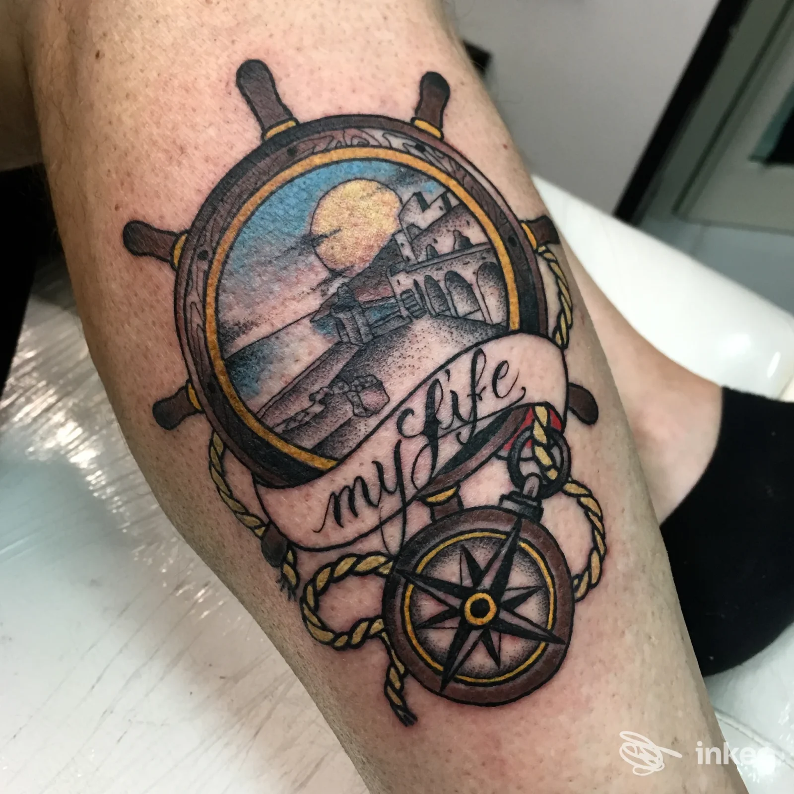Tatuaggio completo su pelle: ruota da barca con paesaggio sullo sfondo e fascia con scritto «my life», decorazioni marittime e corde. Studio Stay True Tattoo Salerno.