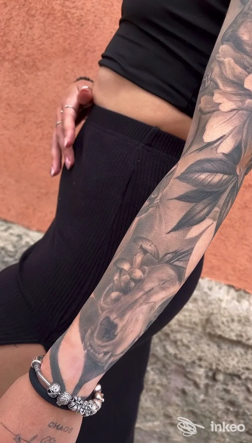 Braccio di una persona con tatuaggio a maniche lunghe: un disegno in bianco e nero che copre quasi completamente l’avambraccio, visibile in primo piano con sfondo muratura color ocra.