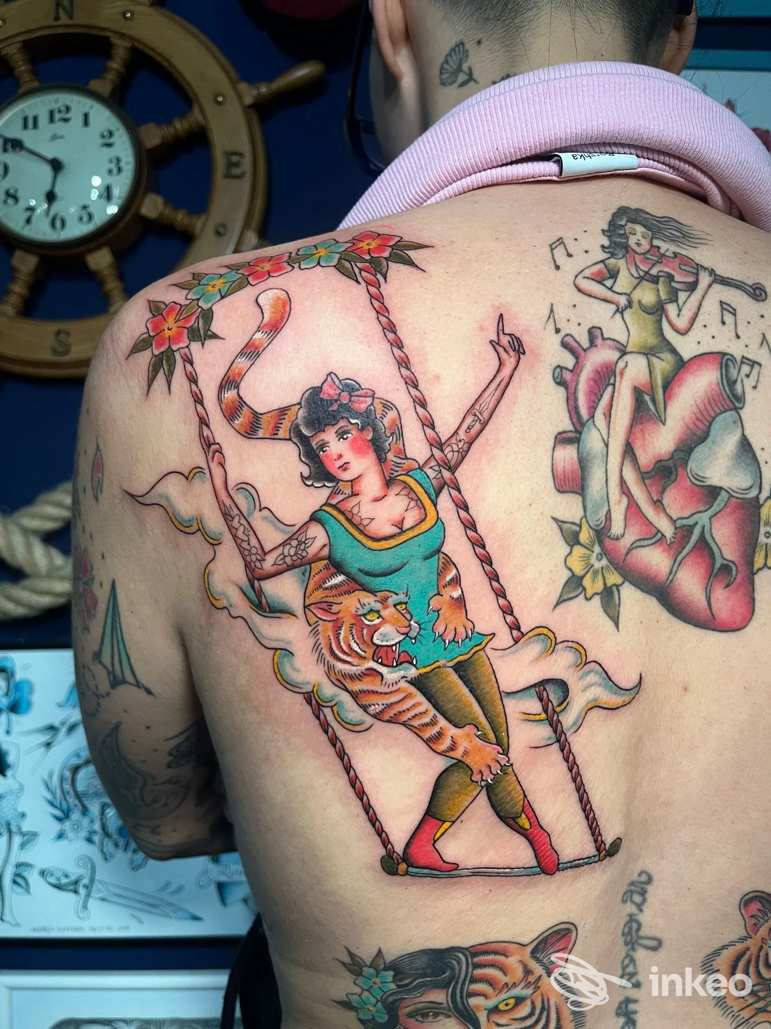 Tattoo sulla schiena di una persona: figura femminile su altalena con tigre e fiori, in stile tradizionale colorato.