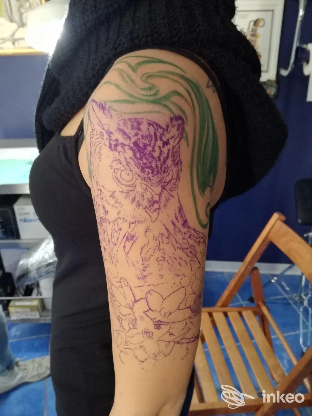 Parte superiore del braccio sinistro, contorni di tatuaggio in fase di outline viola di un animale, con decorazioni verdi sulla spalla, in uno studio.