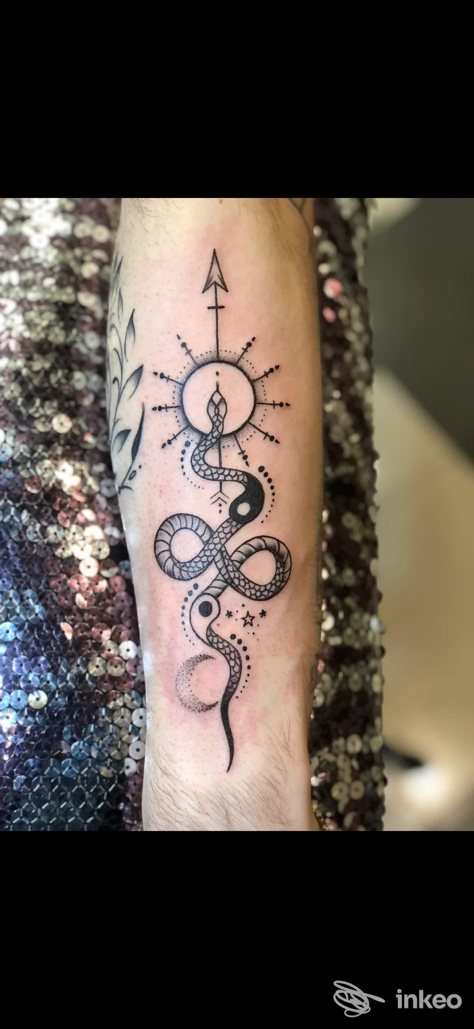 Tattoo su braccio: serpente che si avvolge attorno a una freccia centrale, circondata da un sole stilizzato con raggi. realizzato dallo studio Imprinting Tattoo, Benevento.