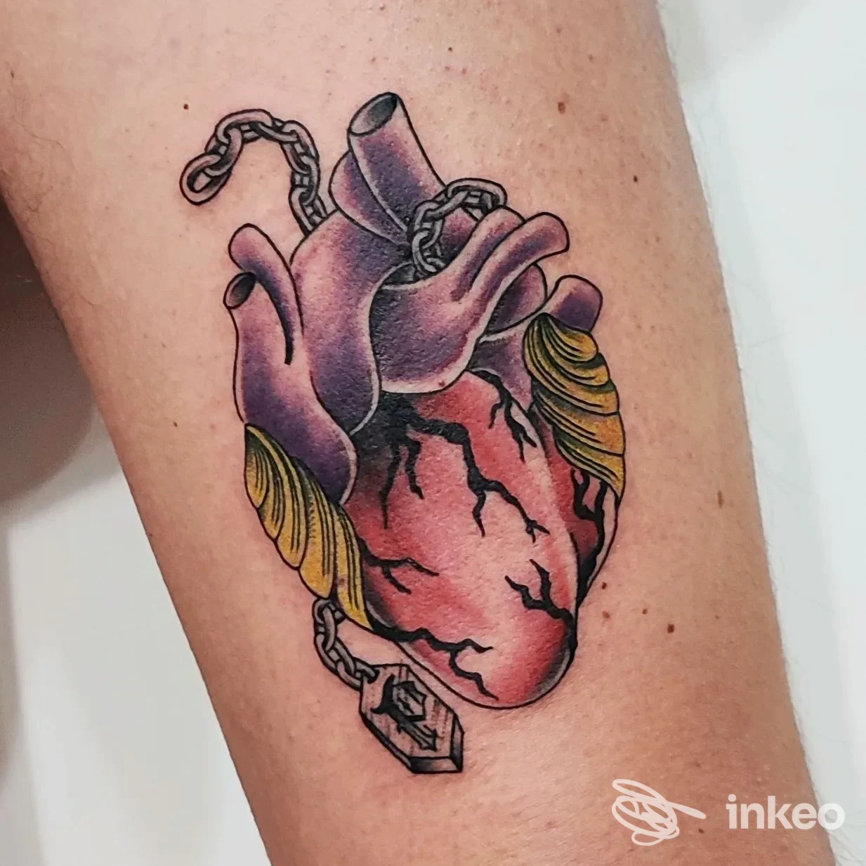Tattoo Colorato di un cuore anatomico con catene e pendente sul braccio, stile realism/vintage, colori vivaci e linee nette.