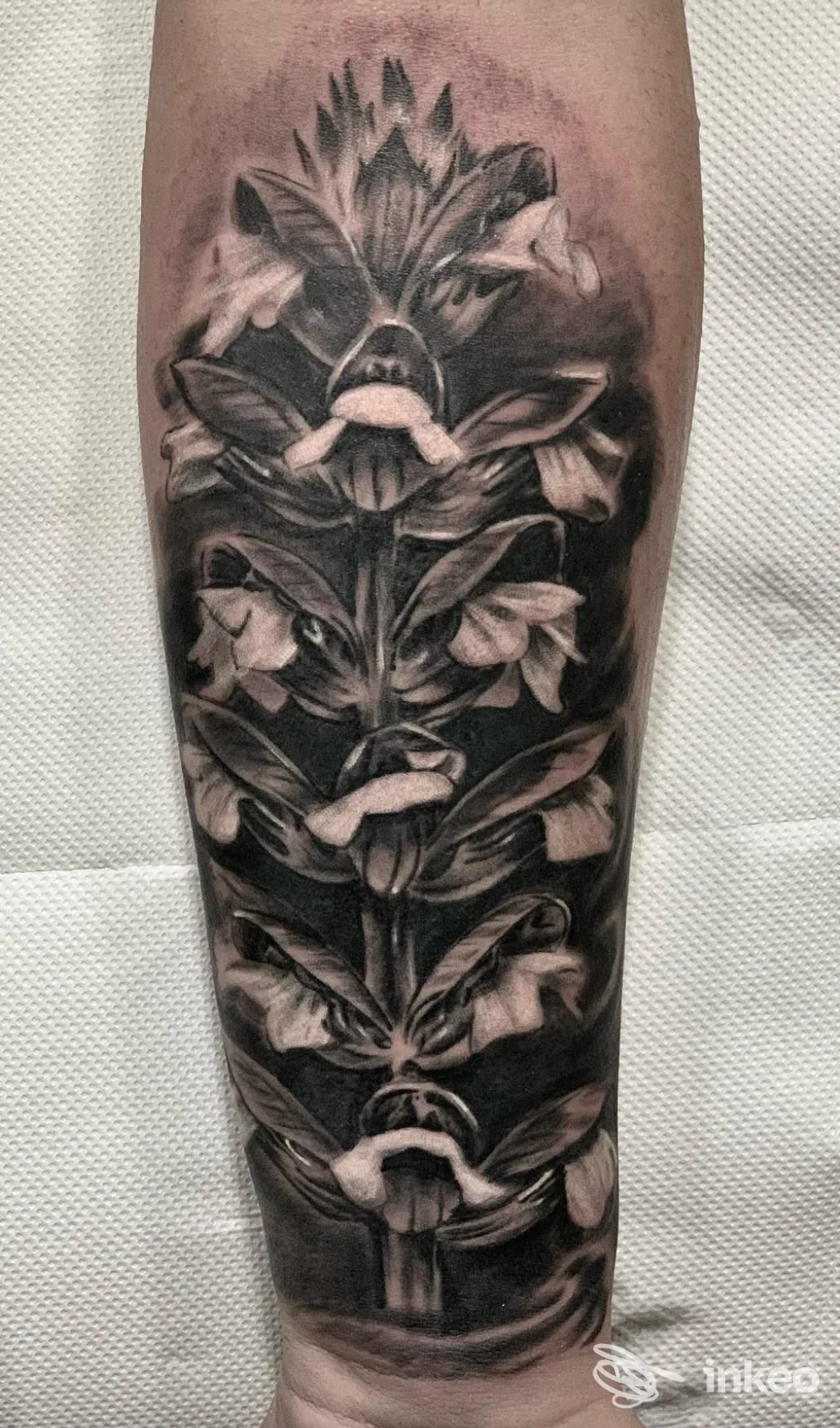 Tattoo realistico in bianco e nero su avambraccio, raffigurante una composizione floreale di fiori chiari su sfondo scuro, realizzata in Barone Tattoo Studio, Marano di Napoli.