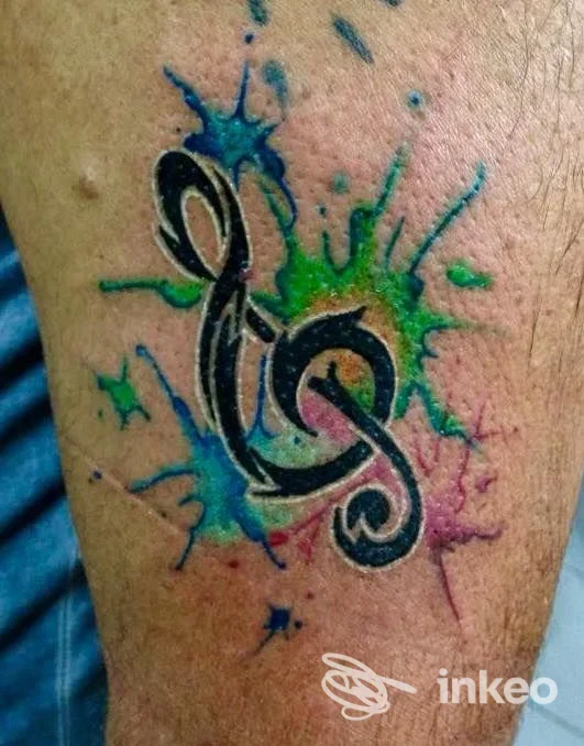 Tatuaggio realizzato presso Tattoo Studio Dario Perna, Napoli: chiave di violino nera con schizzi colorati blu, verde e viola sul contorno della pelle.
