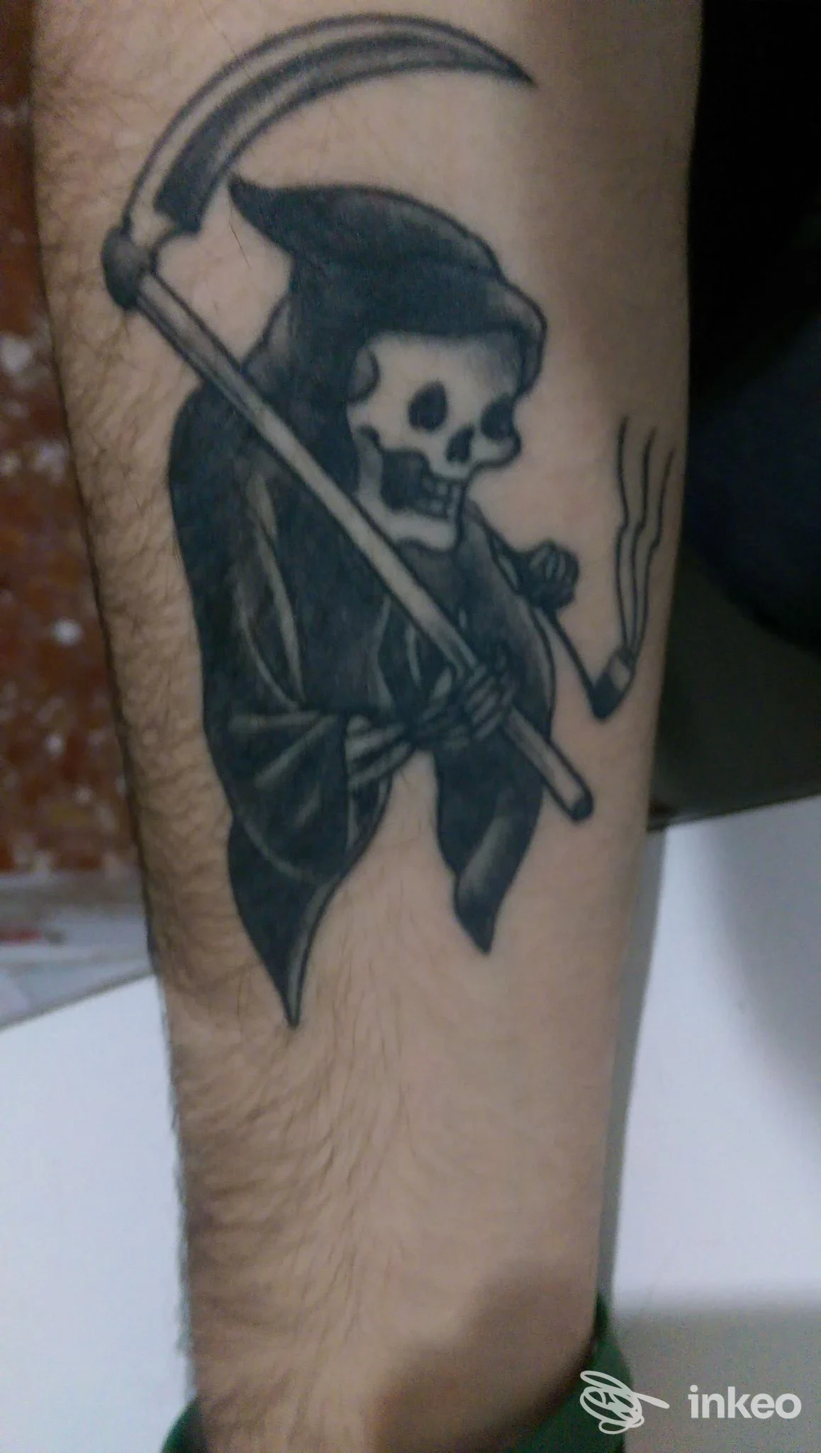 Tatuaggio su braccio raffigurante la Morte con una falce, in stile inchiostrato, colori nero/grigio.