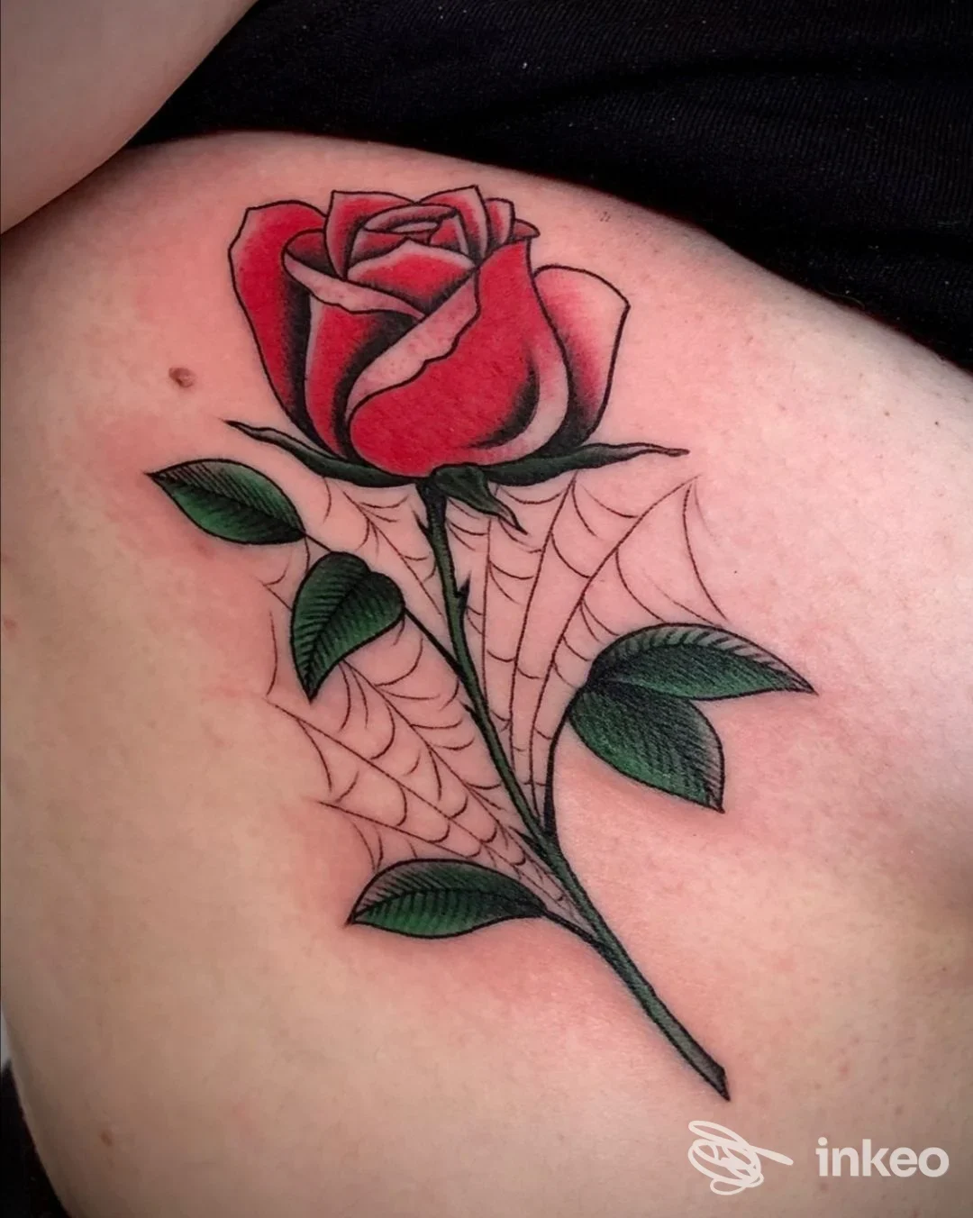 Tatuaggio su pelle raffigurante una rosa rossa con foglie verde scuro, corona di spine e fili di ragnatela; colore e linee definiti, senza testimonianza di contenuti promozionali. Studio Ink in the Soul Tattoo Parlour, Mondragone.