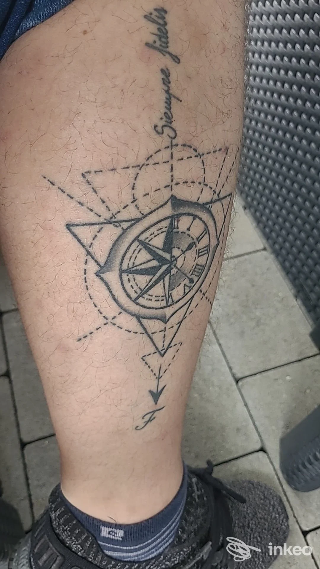 Tattoo geometrico con bussola e triangoli sul polpaccio: linee scure e dettagli intricati, senza viso visibile.