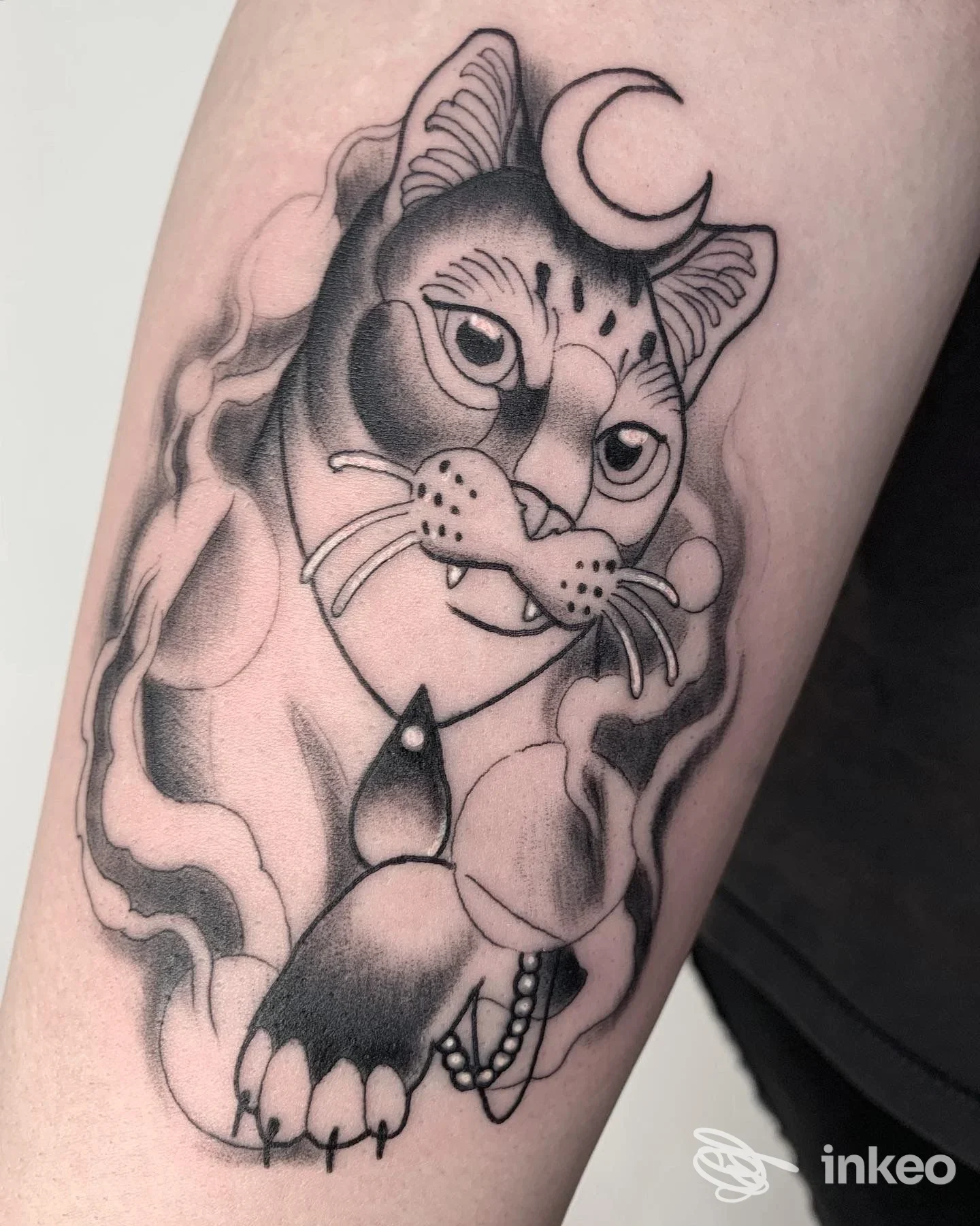 Tatuaggio realistico in bianco e nero raffigurante un gatto con luna crescente sulla fronte, situato sul braccio. stile black and grey con tonalità di chiaroscuro.