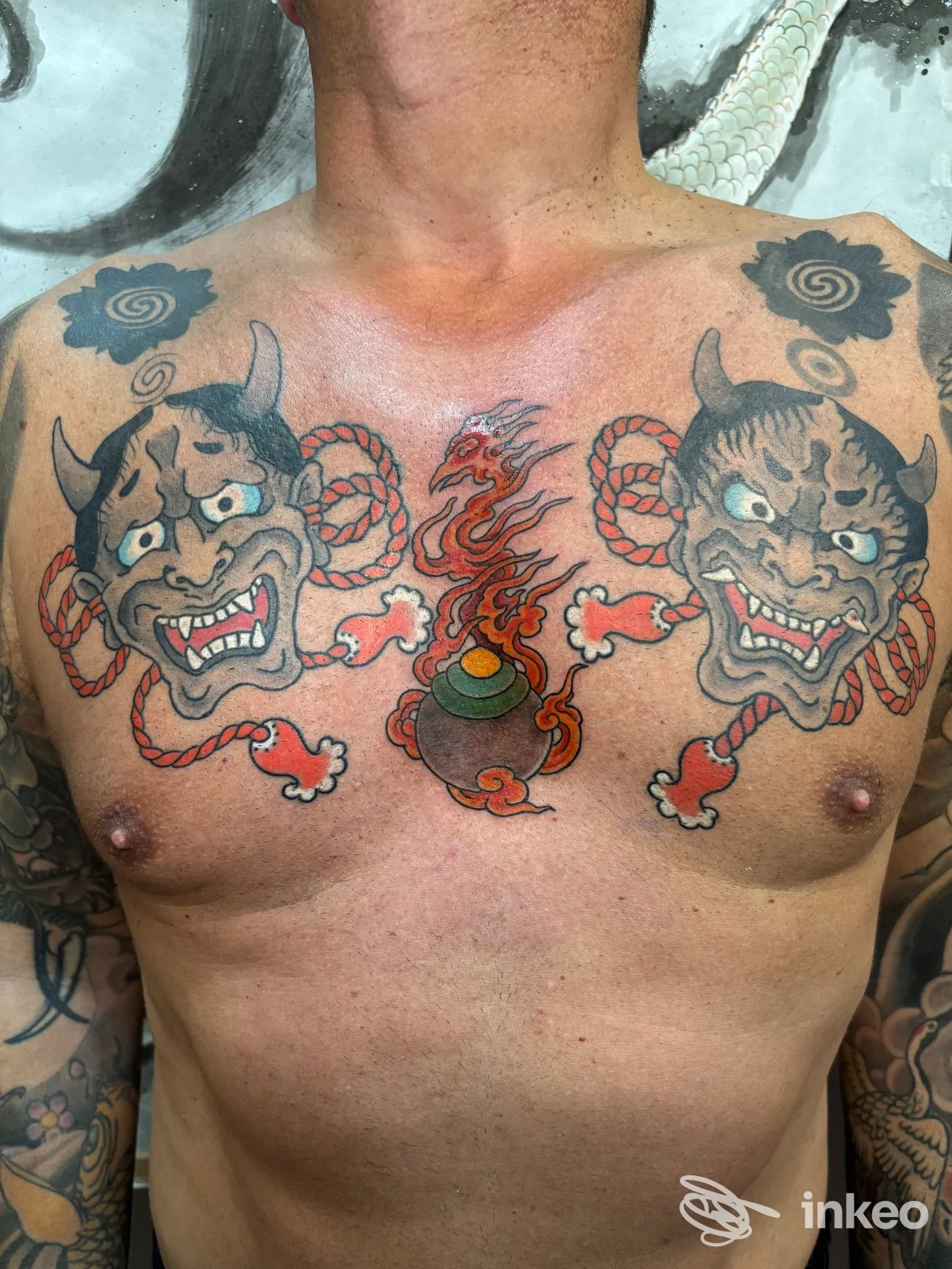 Torso di uomo con tatuaggi: due demoni ai lati con occhi bianchi e zampilli rossi, al centro una ciotola fumante; tatuaggio corporeo reale sul petto, Napoli presso Tattoo Point Studio.