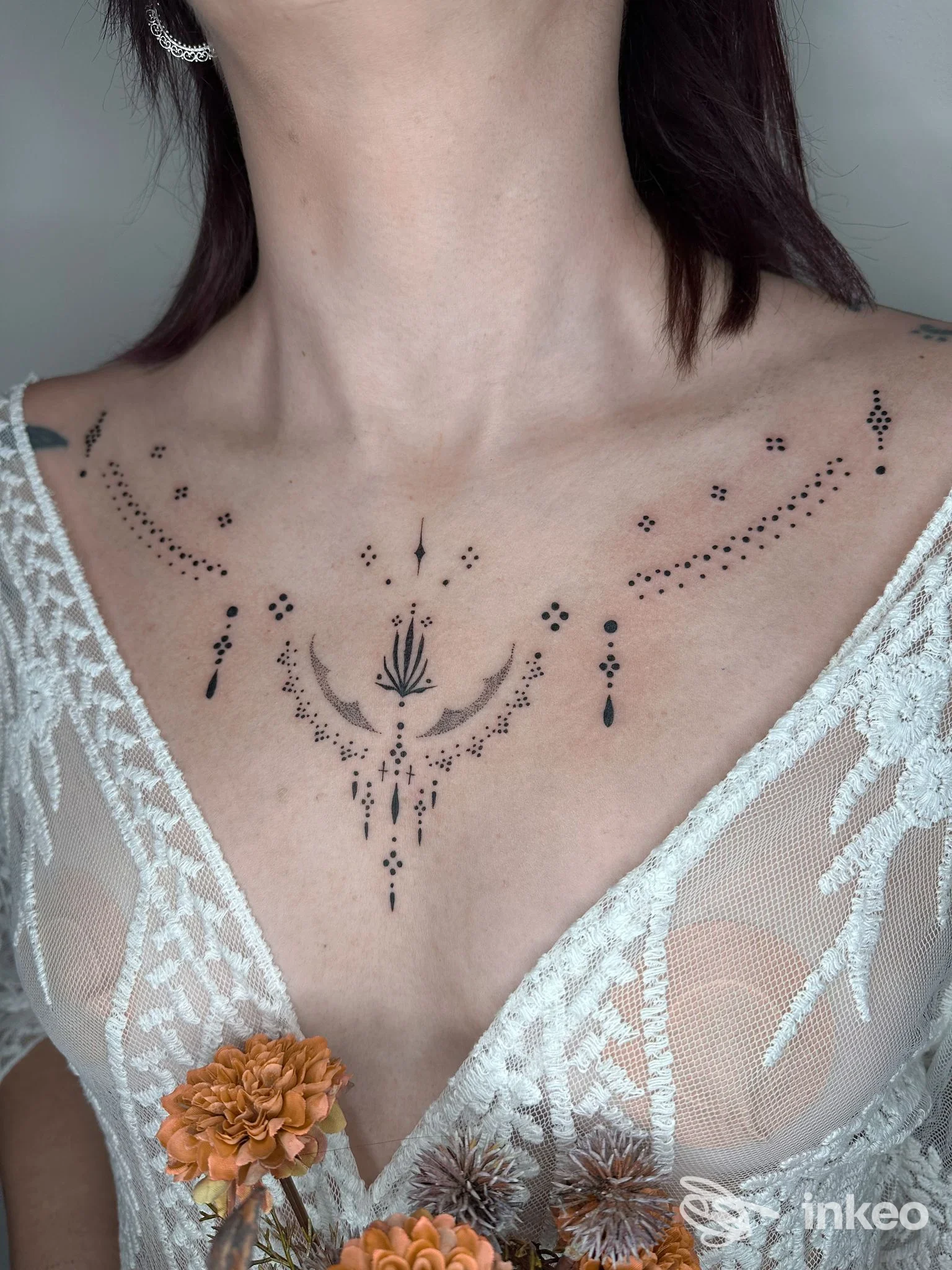Tattoo estetico a puntini e motivi decorativi sul décolleté di una persona, visibile insieme a una scollatura in pizzo bianco.
