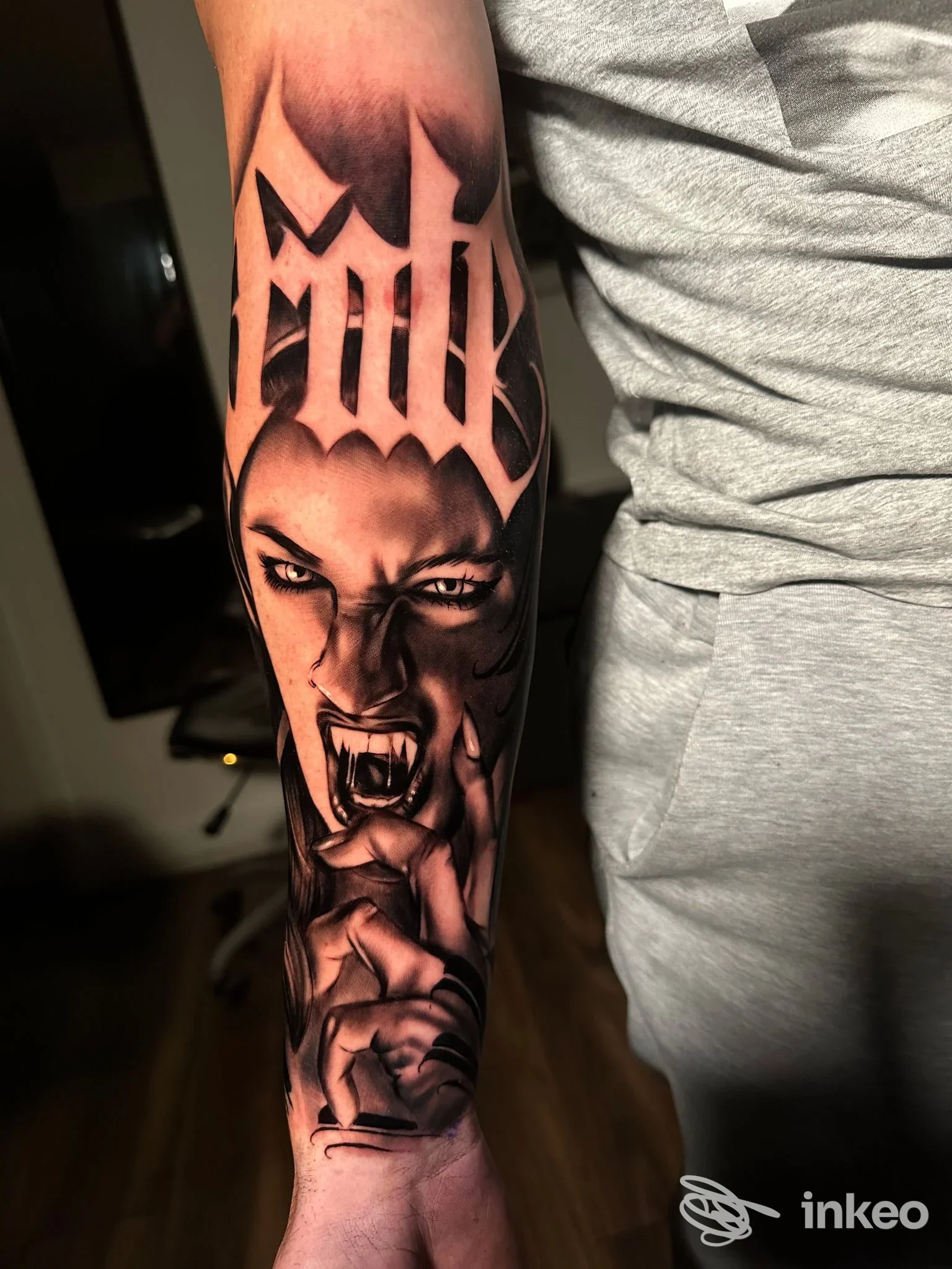 Tattoo a colori su avambraccio raffigurante una figura demoniaca con scritte gotiche in alto; sfondo scuro e contrasti marcati.