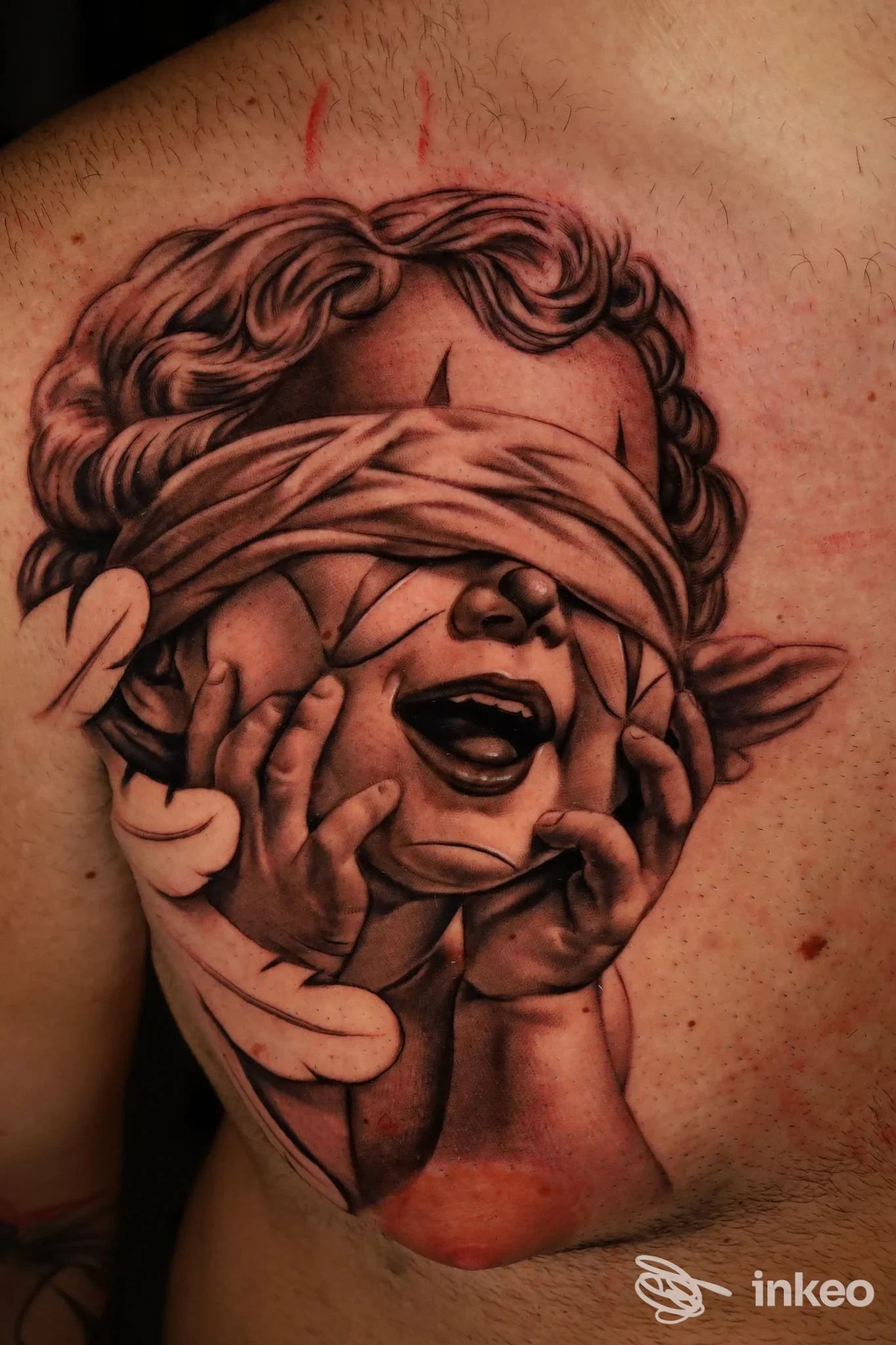 Tattoo realistico su pelle: volto parzialmente coperto da bendaggio, espressione intensa e mani in primo piano, con sfumature e linee simulate con ombre.
