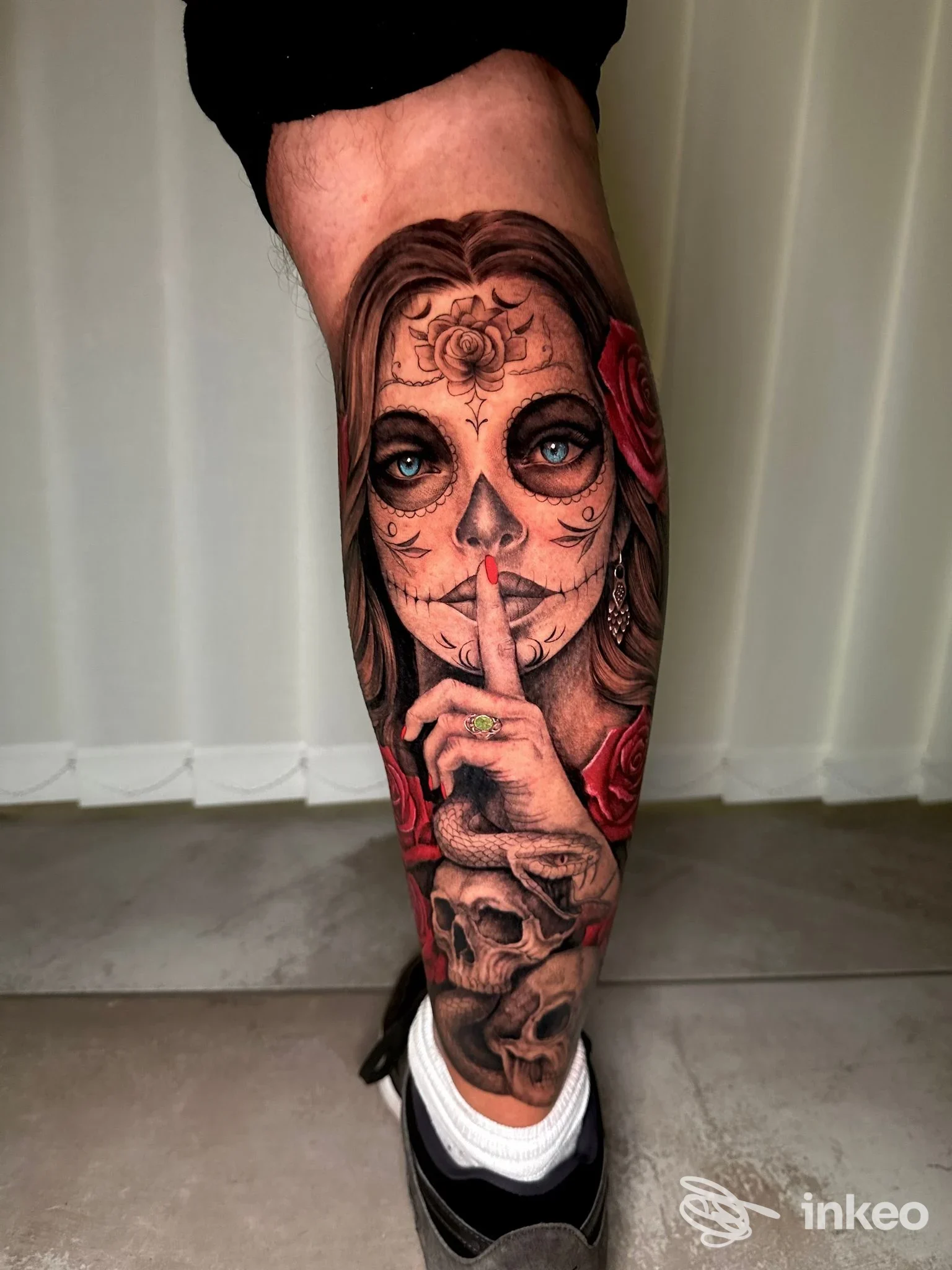Tattoo realistico su gamba destra raffigurante una ragazza con sugar skull, corone di rose e una mano che tocca le labbra, con dettagli scuri e sfumature; visibile una scena di sugar skull stilizzato.