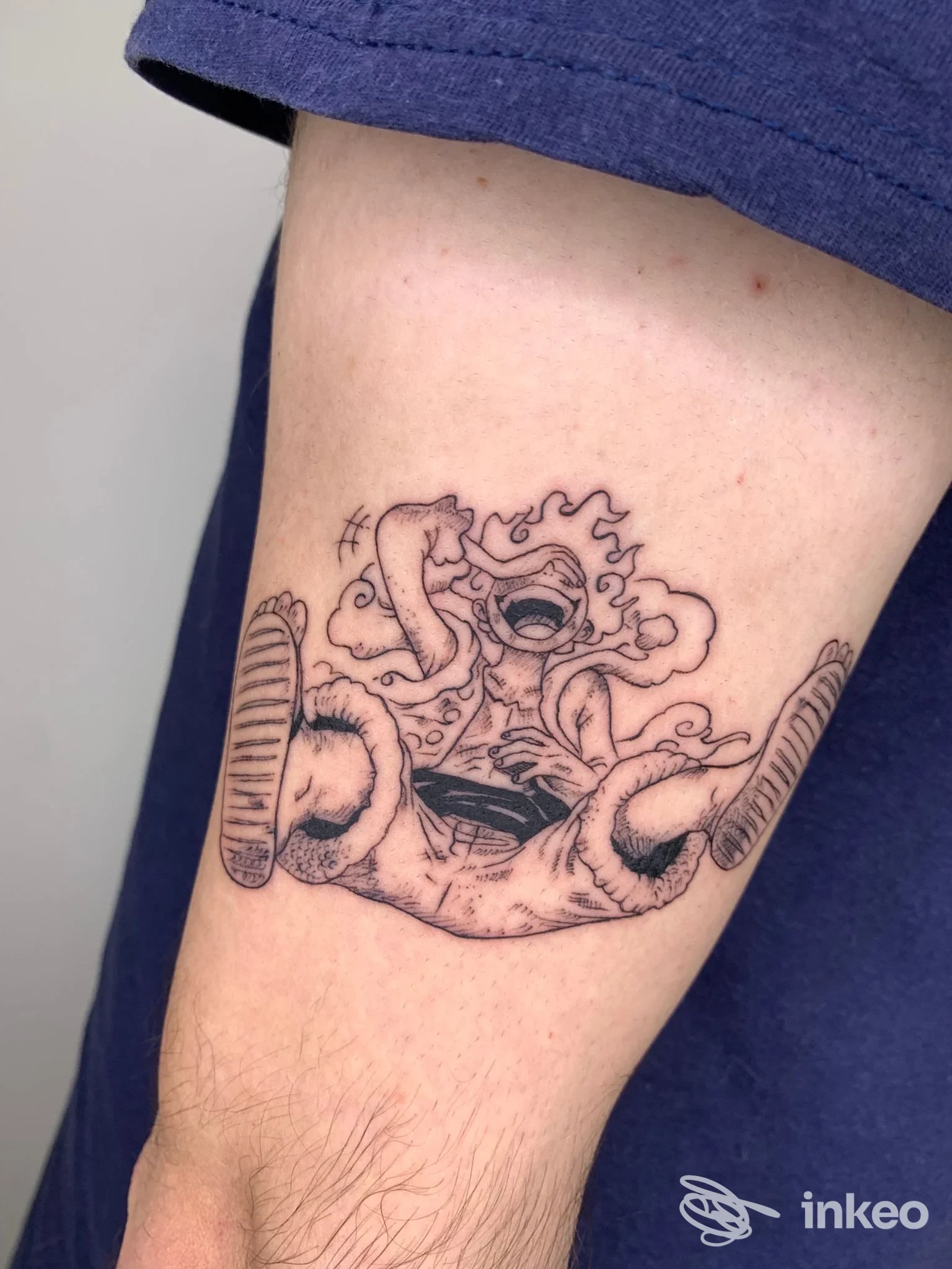 Tatuaggio in stile disegno lineare su braccio: figura nera con contorni netti e riempimenti sfumati, visibile sulla pelle.