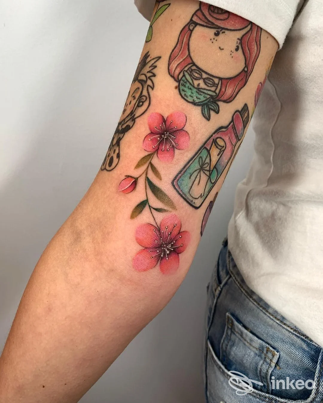 Braccio sinistro con tatuaggi colorati di fiori rosa, stile cartone animato e dettagli vivaci, nessun volto visibile.