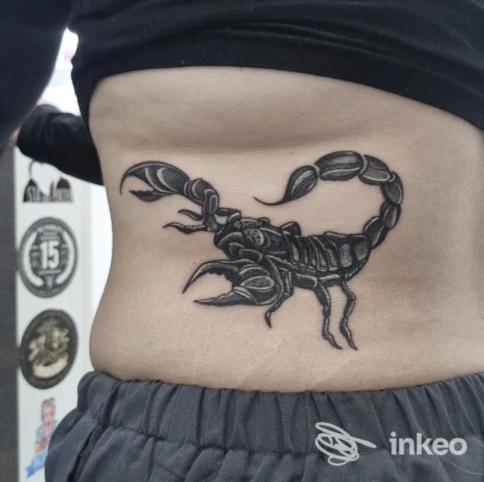 Tattoo di uno scorpione sul fianco sinistro, in nero, con linee nette e dettagli realistici, su pelle nuda della persona.