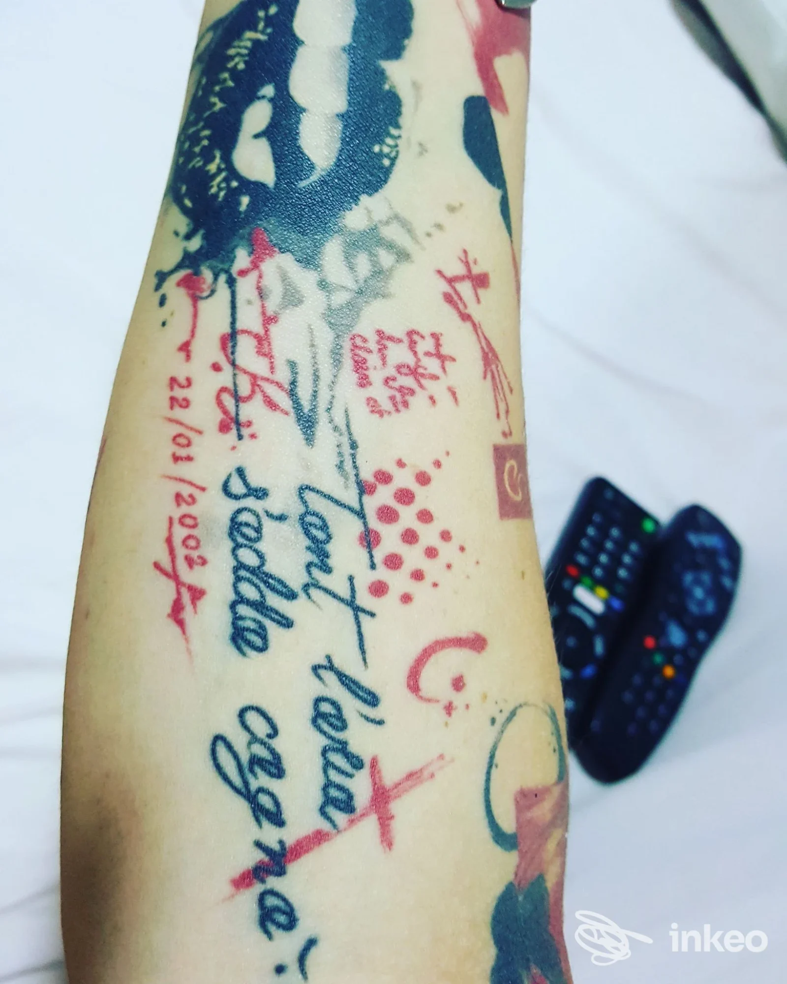 Braccio di una persona con tatuaggi visibili: lettering colorato, pennellate e disegni sul tessuto cutaneo; assente overlay di social e volto non visibile.