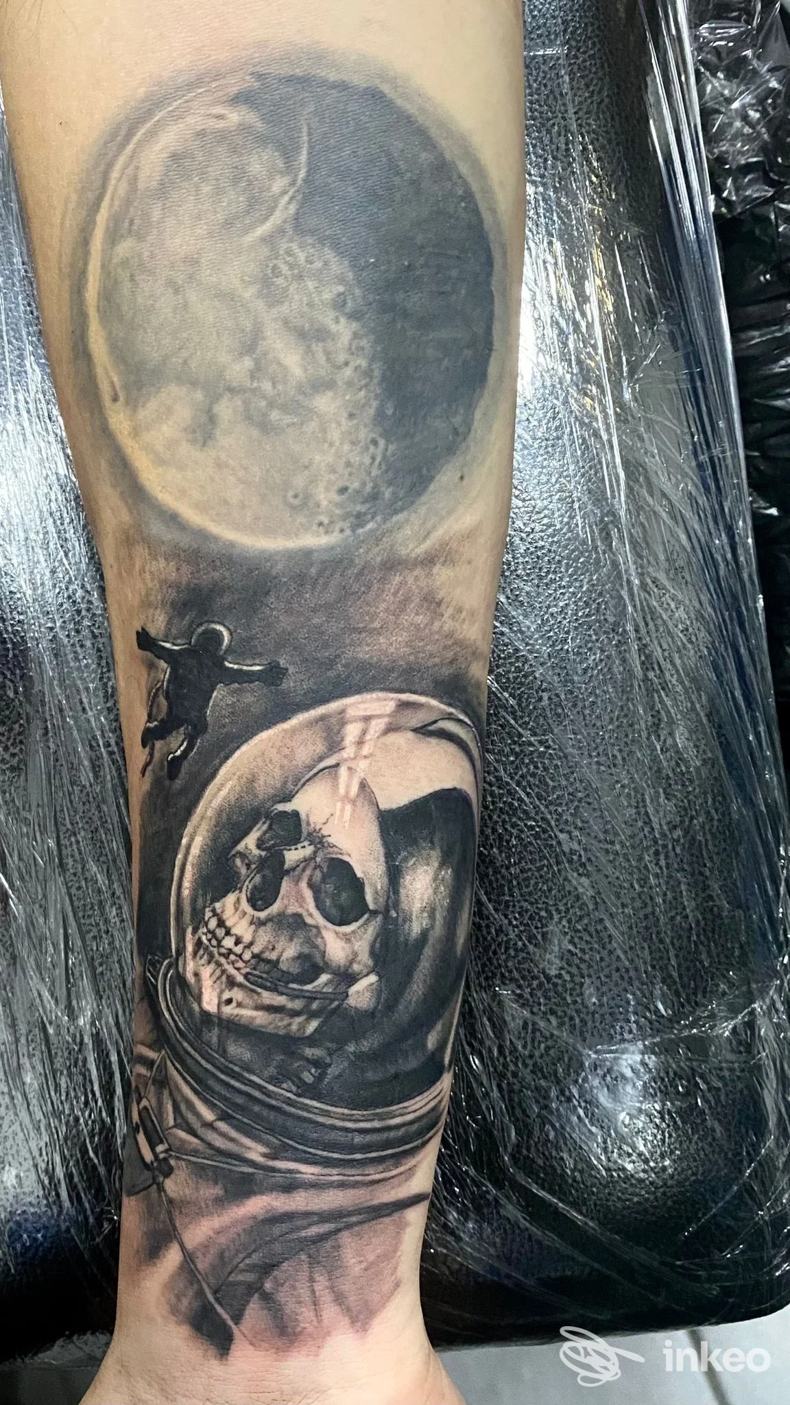 Tatuaggio realistico sul braccio raffigurante un teschio in casco astronautico, con tonalità scure e sfumature grigie, visibile in primo piano.