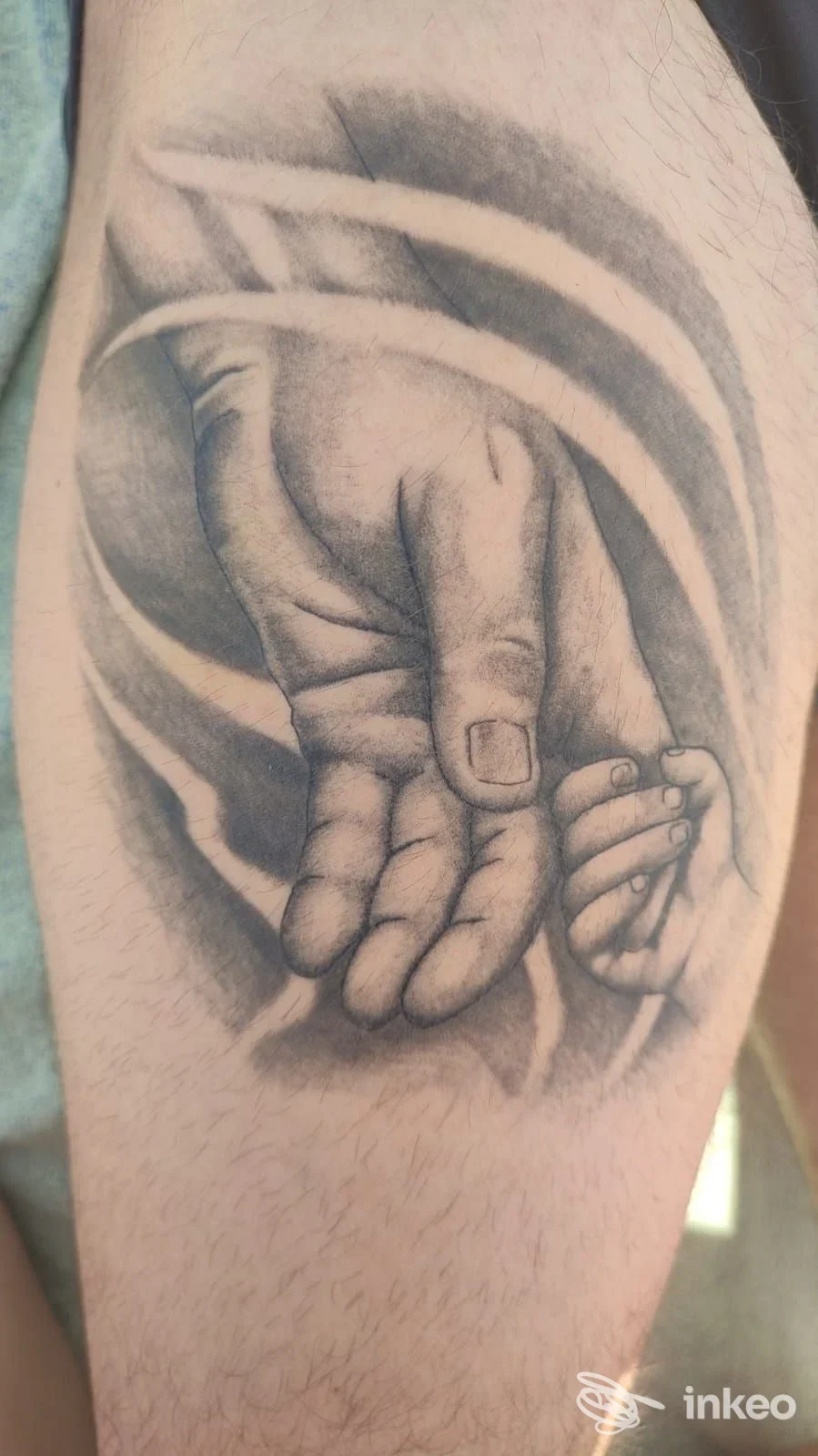 Tattoo realistico in bianco e nero su braccio: mani di adulto e bambino avvicinate, con sfumature delicate e ombreggiature; firma visibile della pelle integra.