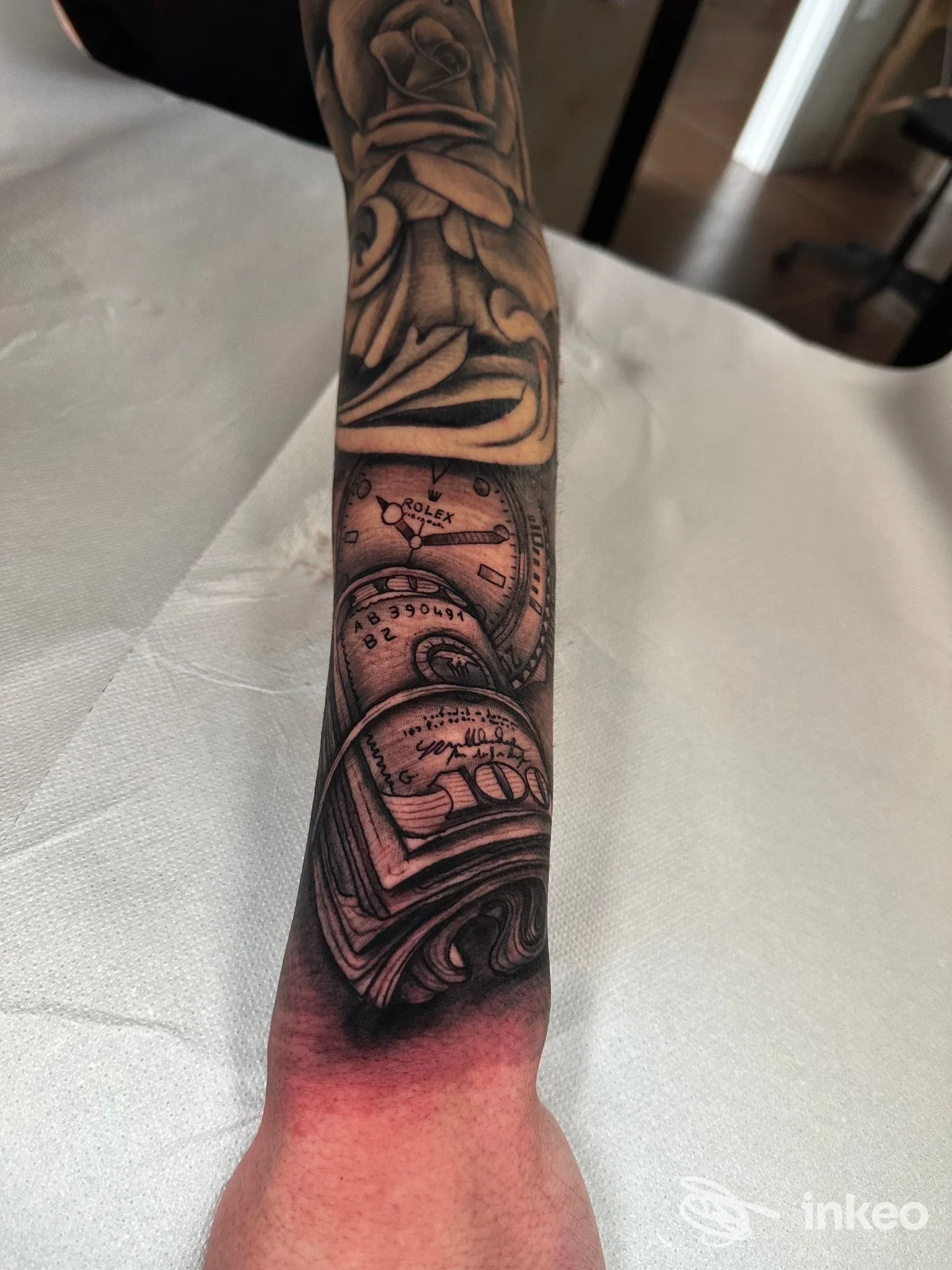 Braccio con tatuaggio realistico in tonalità nere/grigie: orologio e ingranaggi avvolti da linee fluide, eseguito sulla pelle, senza viso visibile.
