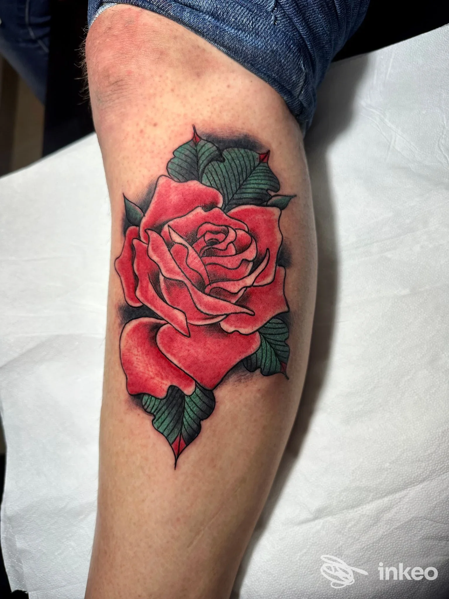 Tatuaggio di una rosa rossa su braccio, con foglie verdi, realizzato sulla pelle, visibile l'artwork corporeo senza volto umano.