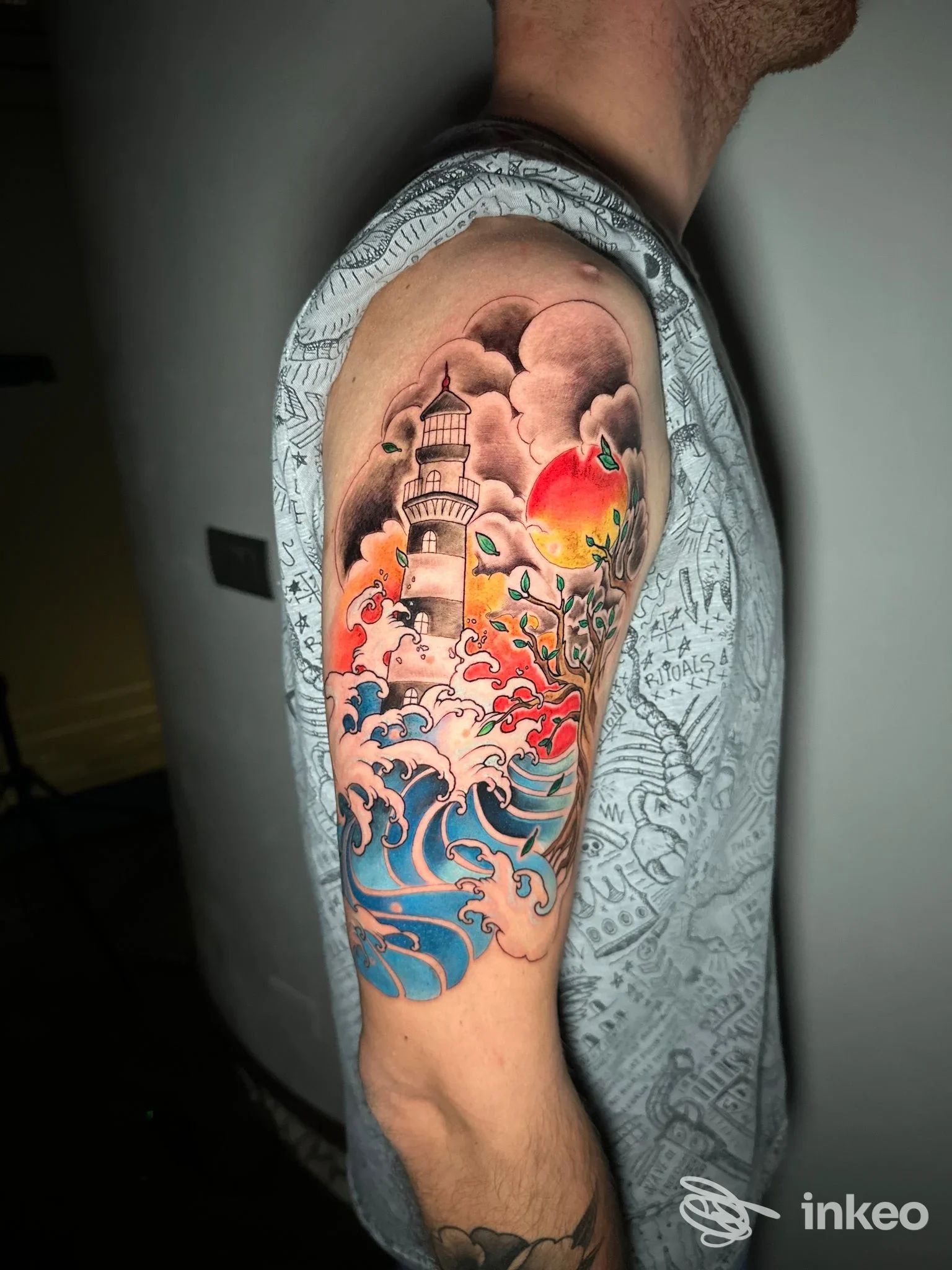Tattoo colorato sul braccio di un uomo raffigurante un faro, onde e sole, realizzato sulla pelle.