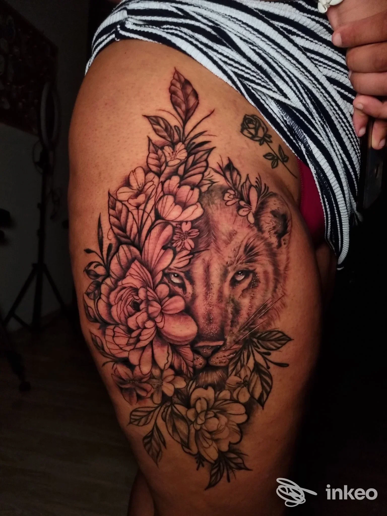 Tattoo visibile sulla coscia: ritratto di leone intrecciato con fiori, eseguito sulla pelle, con colori sobri e linee pulite presso Bahia Ink Tattoo Shop a San Nicola la Strada.