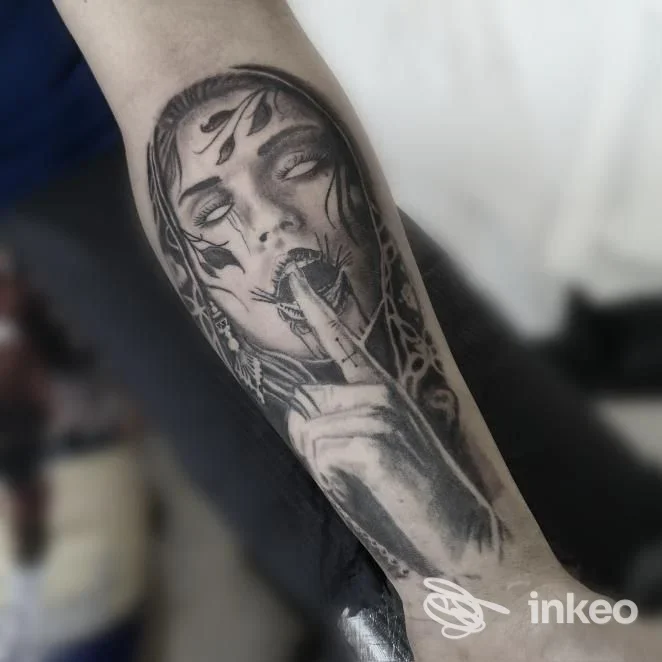 Tatuaggio in bianco e nero sull'avambraccio raffigurante una figura femminile stilizzata con dettagli muscolari e foglie, visibile su pelle reale