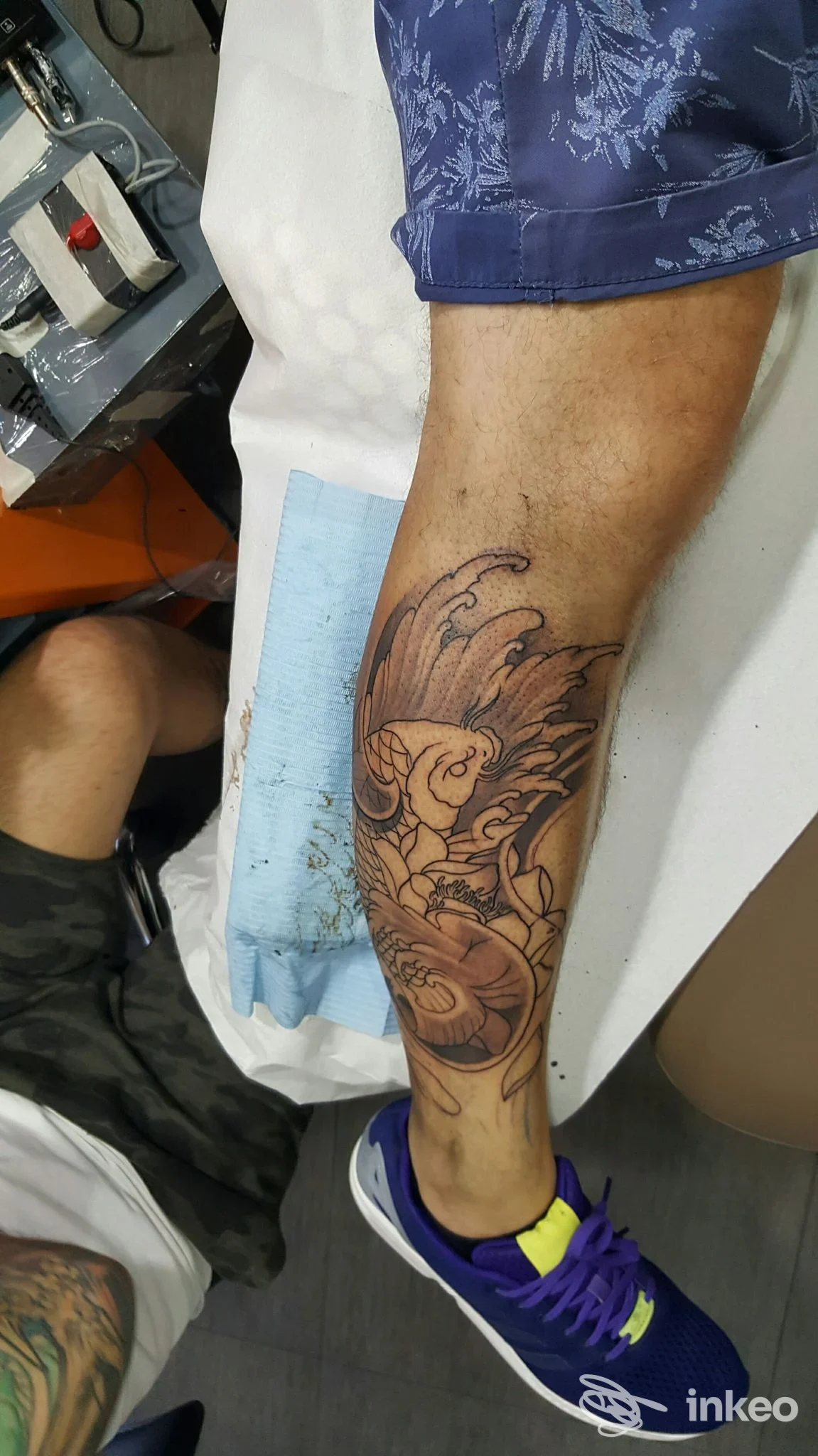 Tattoo visibile sull'avambraccio, disegno a linea nera di un uccello stilizzato con ali aperte, realizzato sulla pelle; sfondo superficie clinica, calzini blu con scarpa viola; studio Vinz Art Tattoos, Salerno.