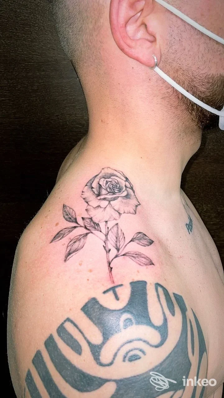 Veduta laterale del collo di un uomo con un tatuaggio a rosa sul collo e altre parti di tatuaggi visibili sulla spalla.