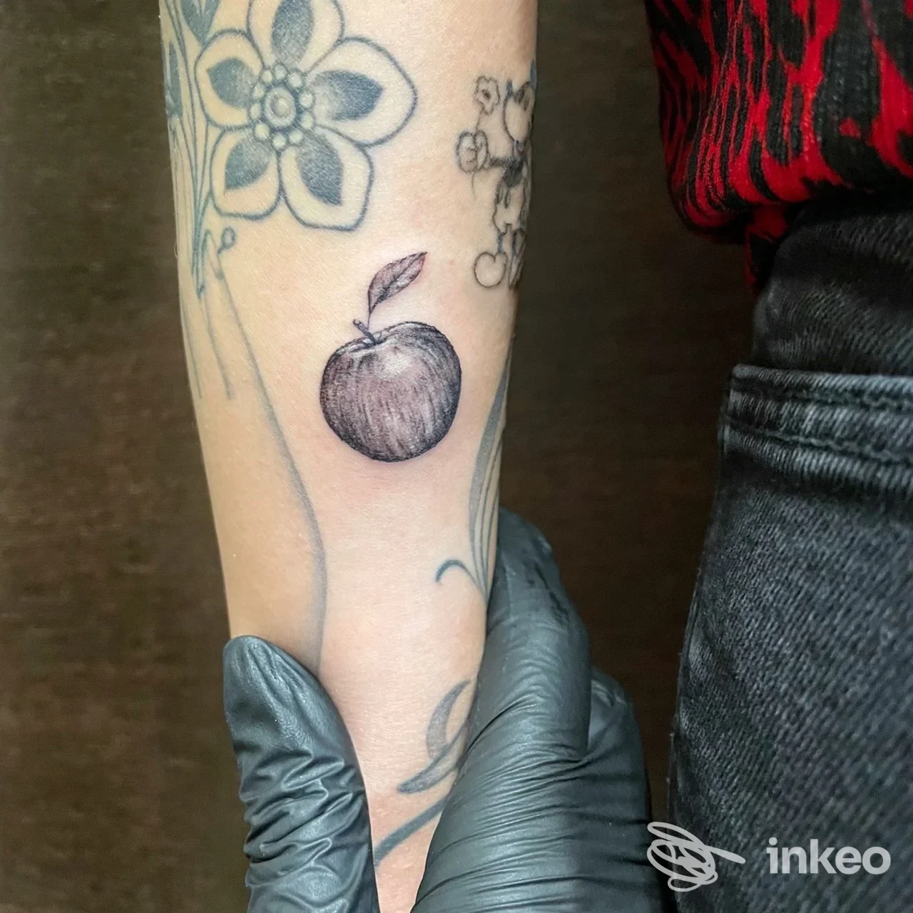 Braccio di una persona con tatuaggio di mela e fiori visibile in primo piano, realizzato sulla pelle.