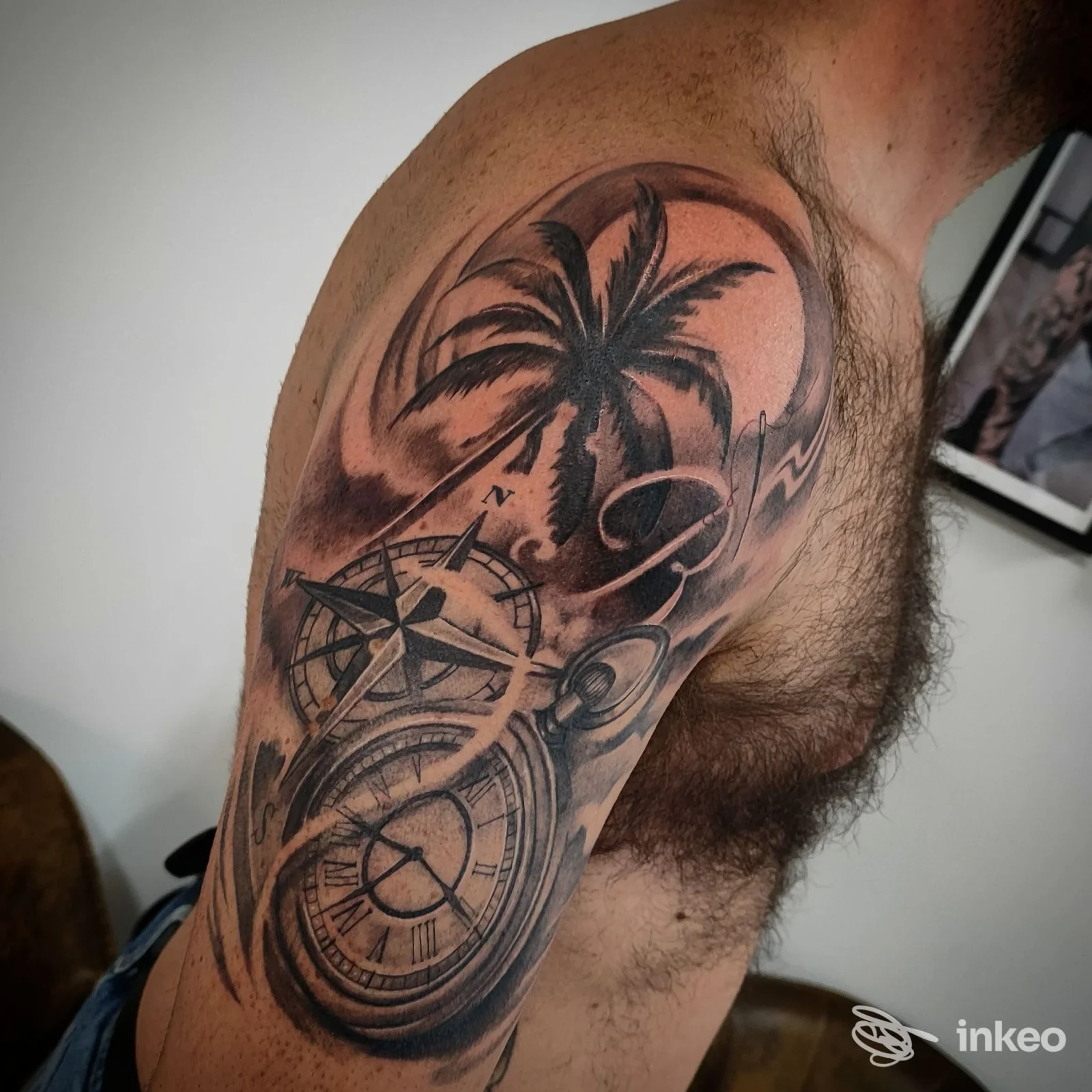 Tattoo sul braccio sinistro raffigurante una palma e una bussola con ombreggiature realistiche, visibile su pelle maschile, senza volto visibile o overlay sociale.